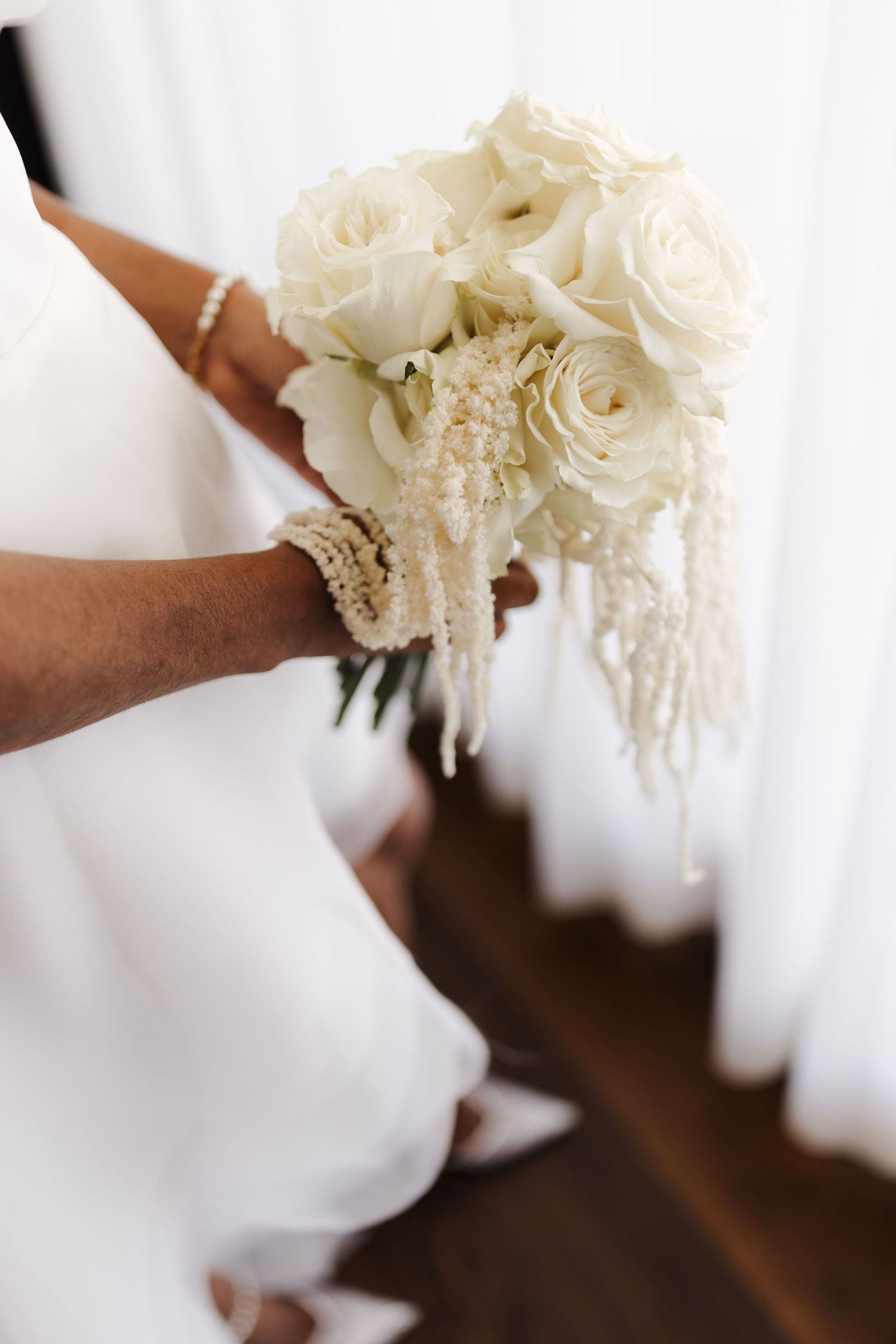 Close-up of a bridal bouquet of white roses with pearl-like trailing amaranthus held by the bride.