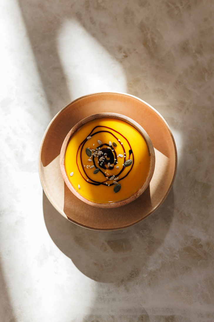 Top view of a golden mango dessert tart with chocolate drizzle in a wooden bowl.