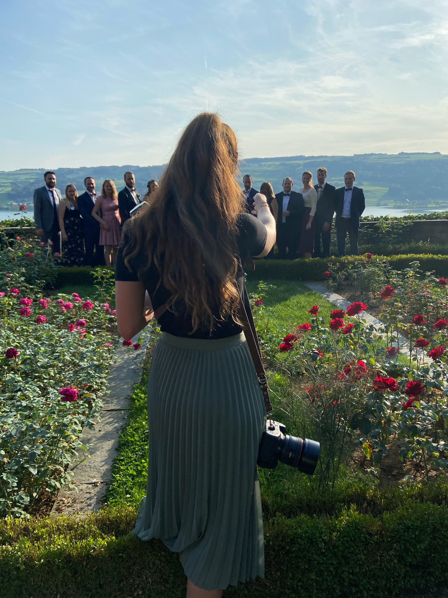 Female photographer with camera photographing a group in a scenic rose garden at golden hour.