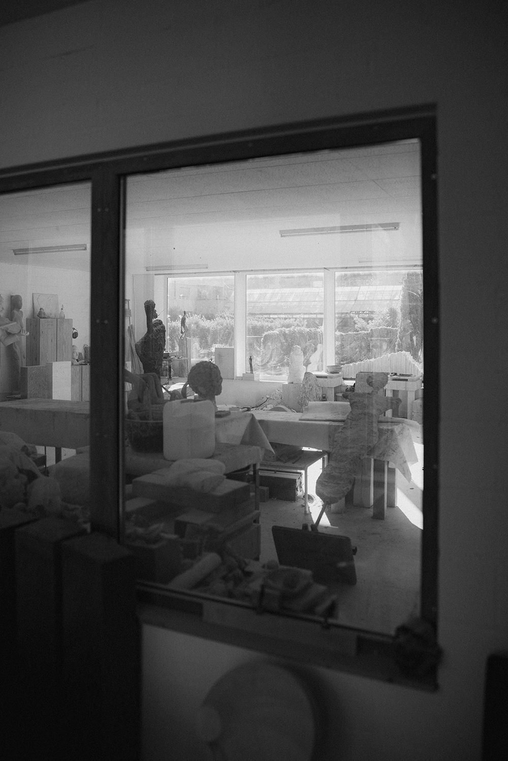 Black and white photograph looking through a window into a bright sculptor's studio with various artworks.