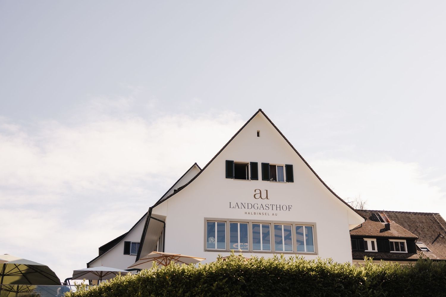 Exterior of white building with gabled roof displaying sign for ai Landgasthof against cloudy sky.