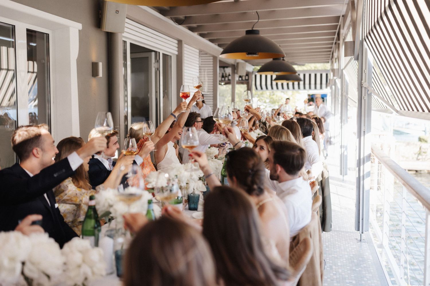 Wedding guests raising glasses in a celebratory toast at a long decorated reception table.