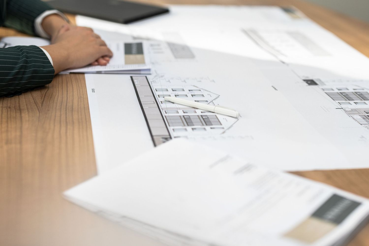 Architectural floor plans and design blueprints spread on a wooden desk during a professional planning meeting.