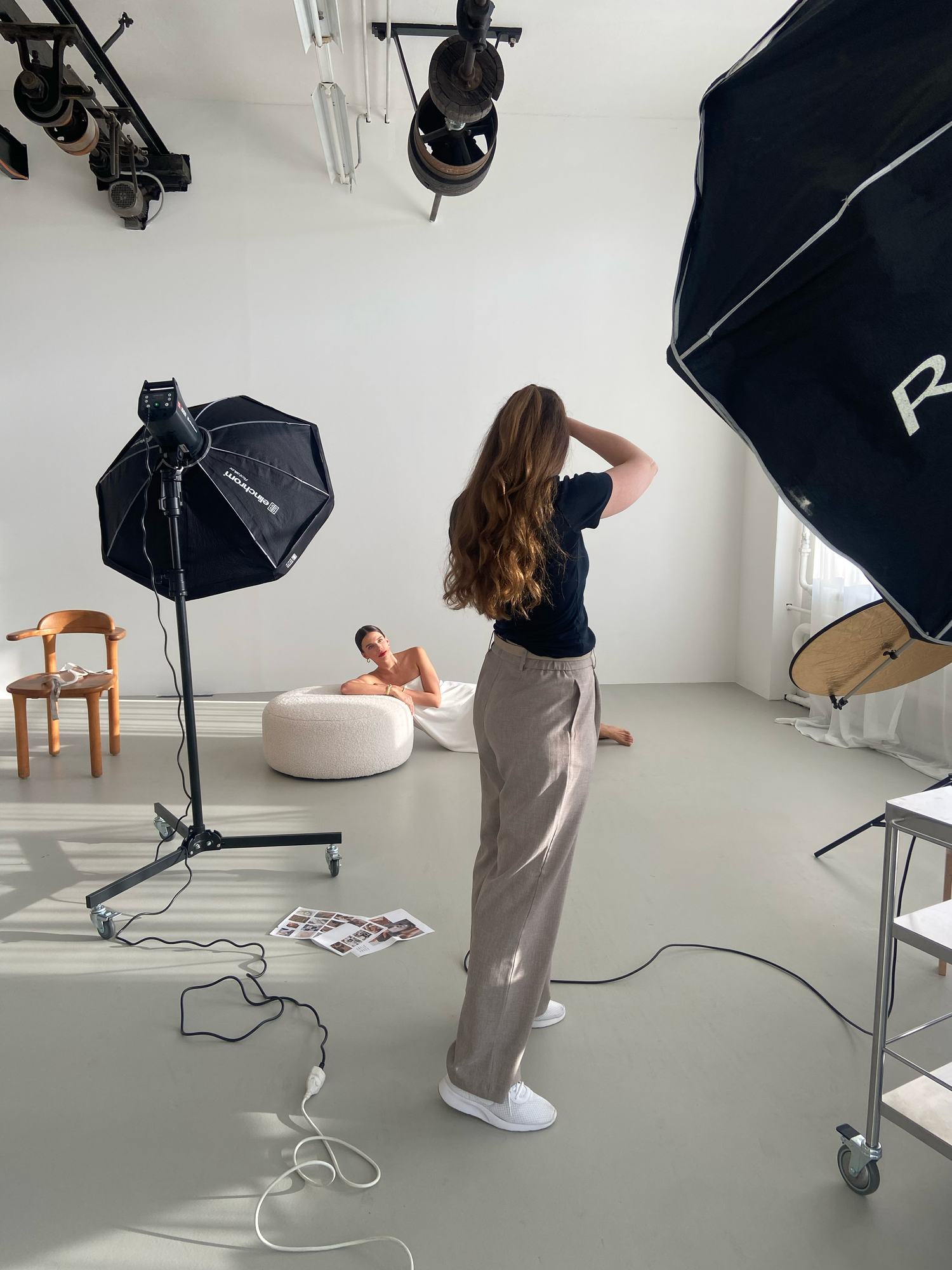 Photographer directing a model in a professional photo studio with softbox lighting equipment.