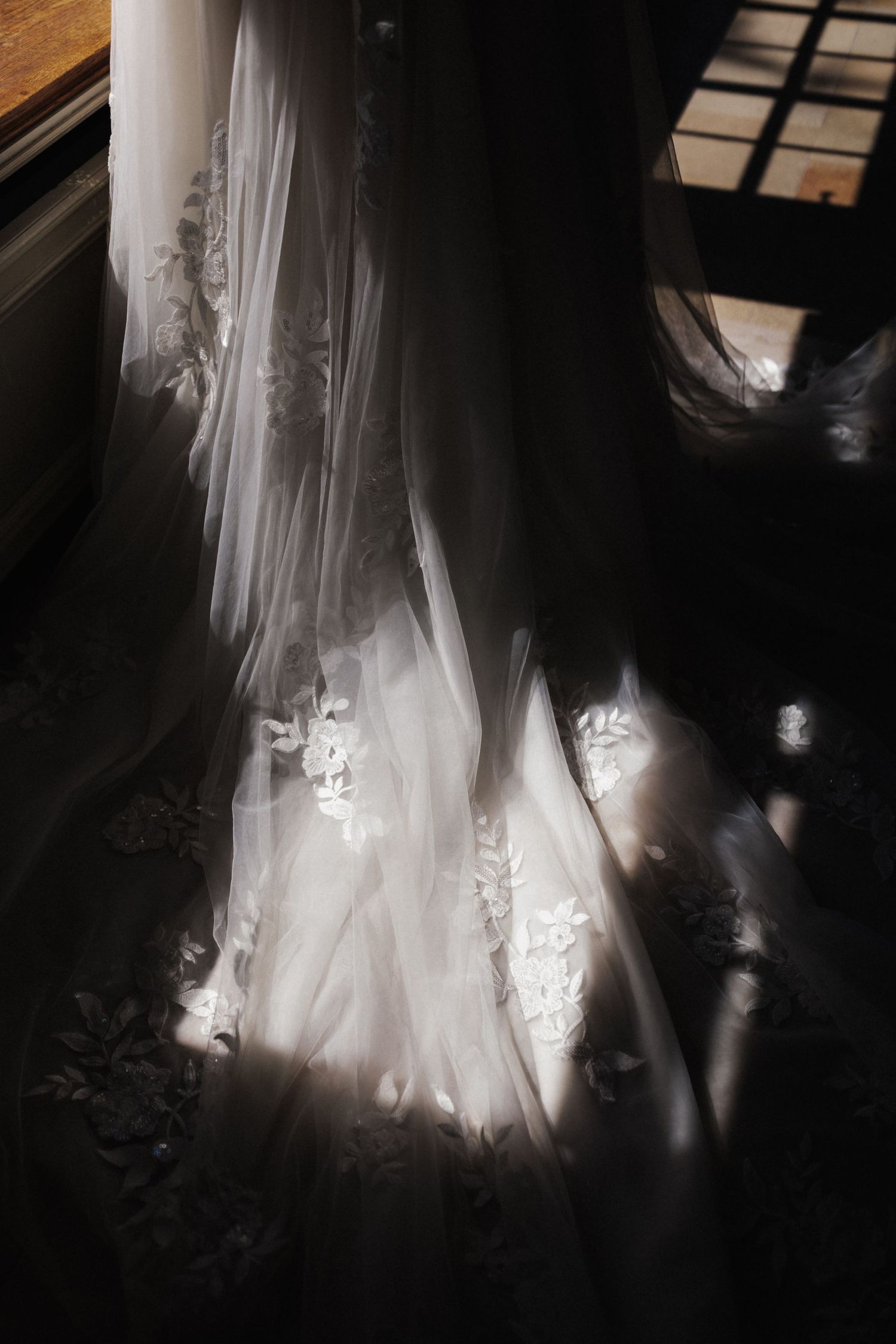 Dramatic moody close-up of a wedding gown train with lace appliques in shadow and light.