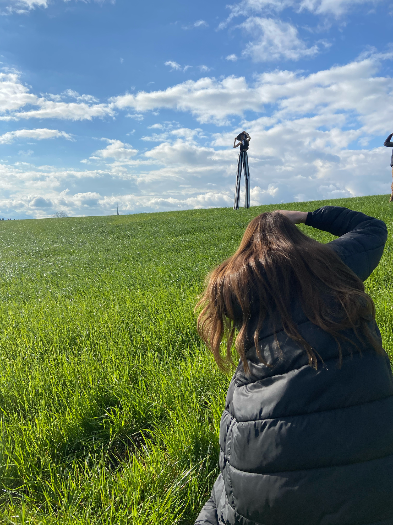 Photographer sitting in green field observing a camera on tripod under a blue cloudy sky.