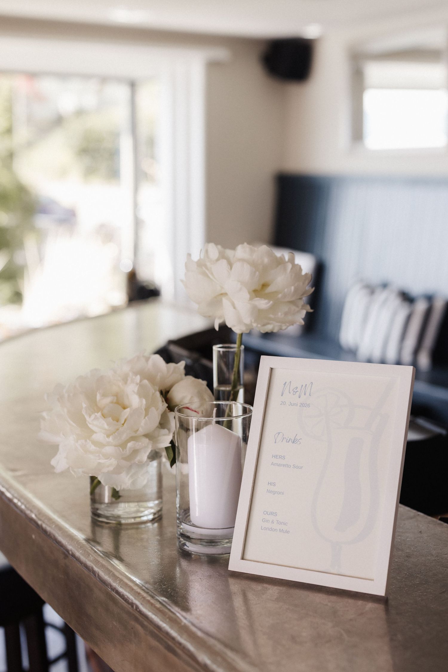White peony floral arrangements and framed wedding menu displayed on marble bar counter.