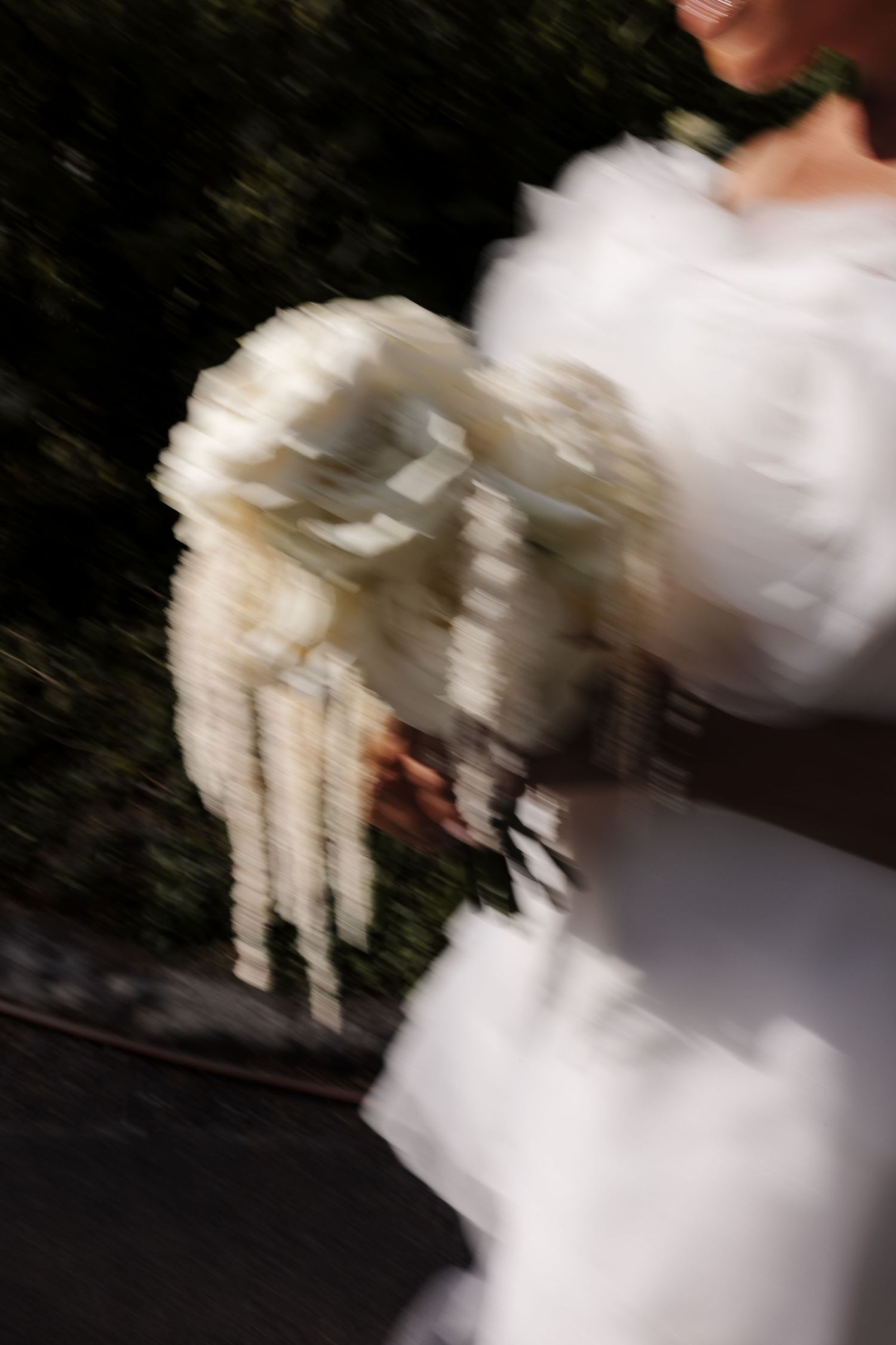 Motion blur artistic wedding photo of bride in white dress carrying white floral bouquet.