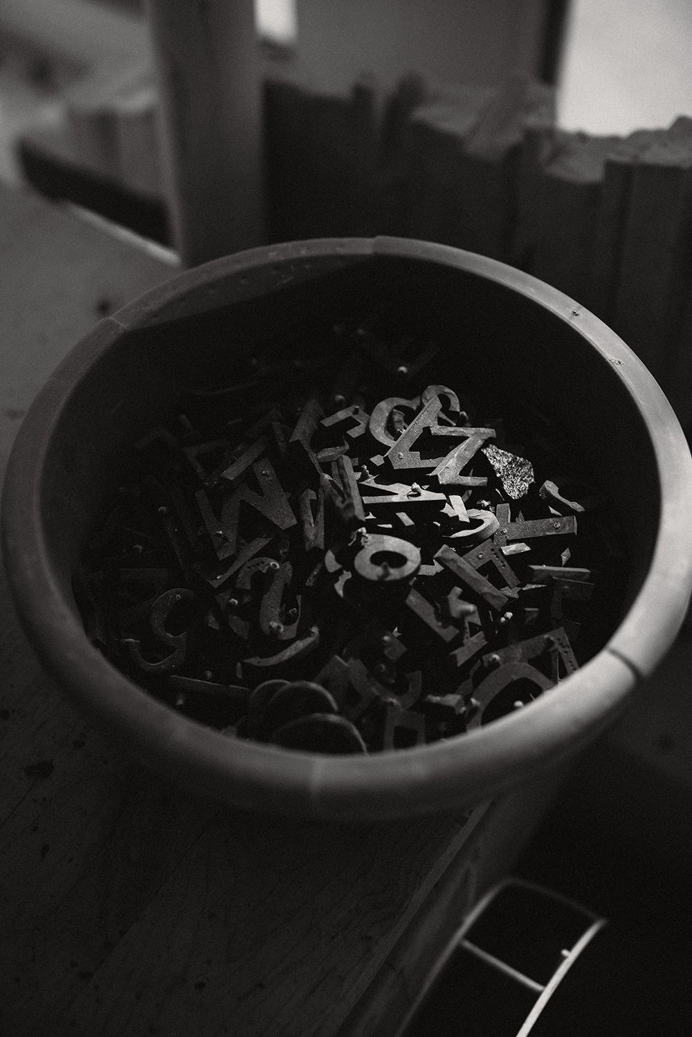 Bucket filled with metal letter stamps and typographic tools in a stone carving workshop.
