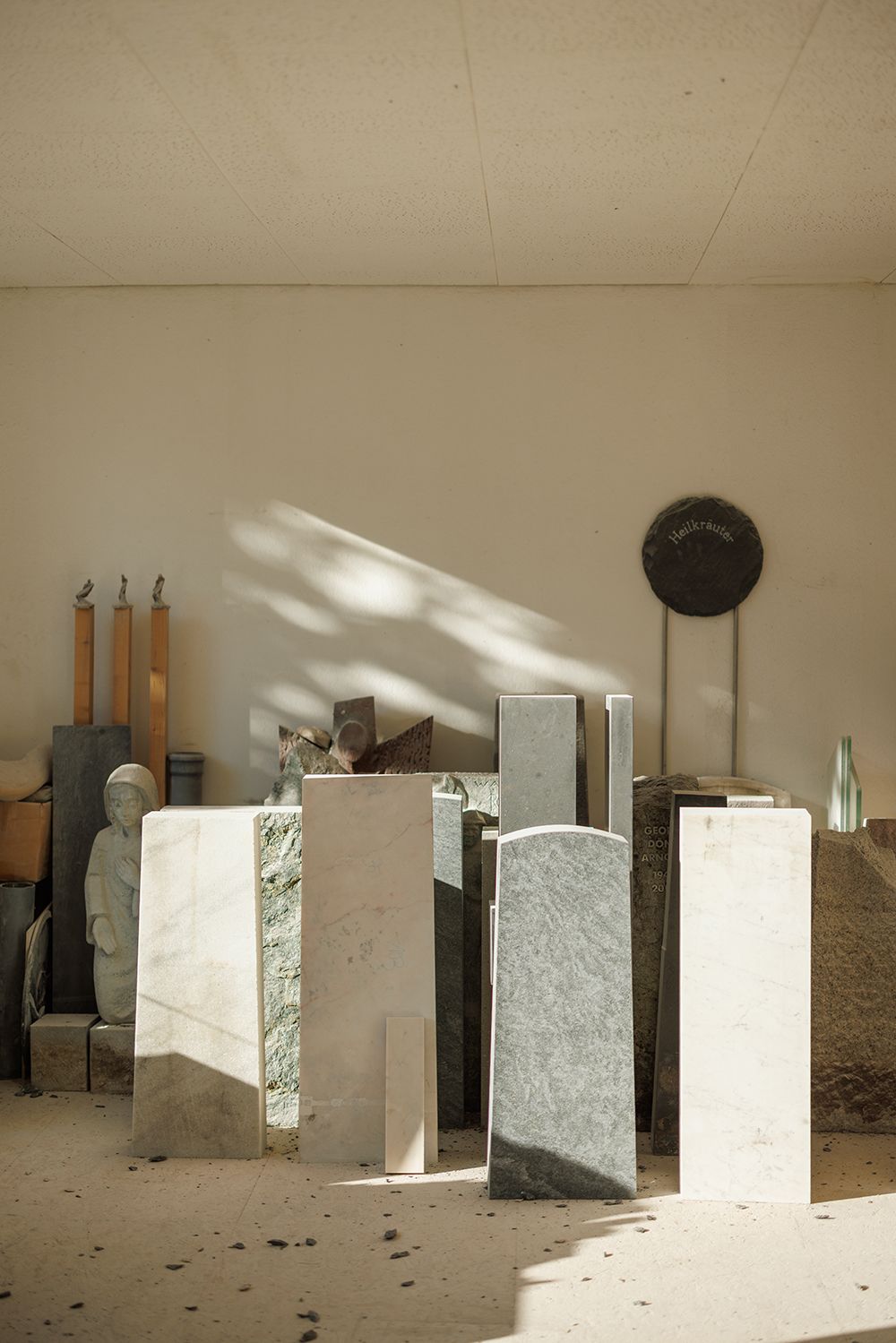 Sunlit stone sculptor's studio with marble slabs and granite blocks arranged on a dusty floor.