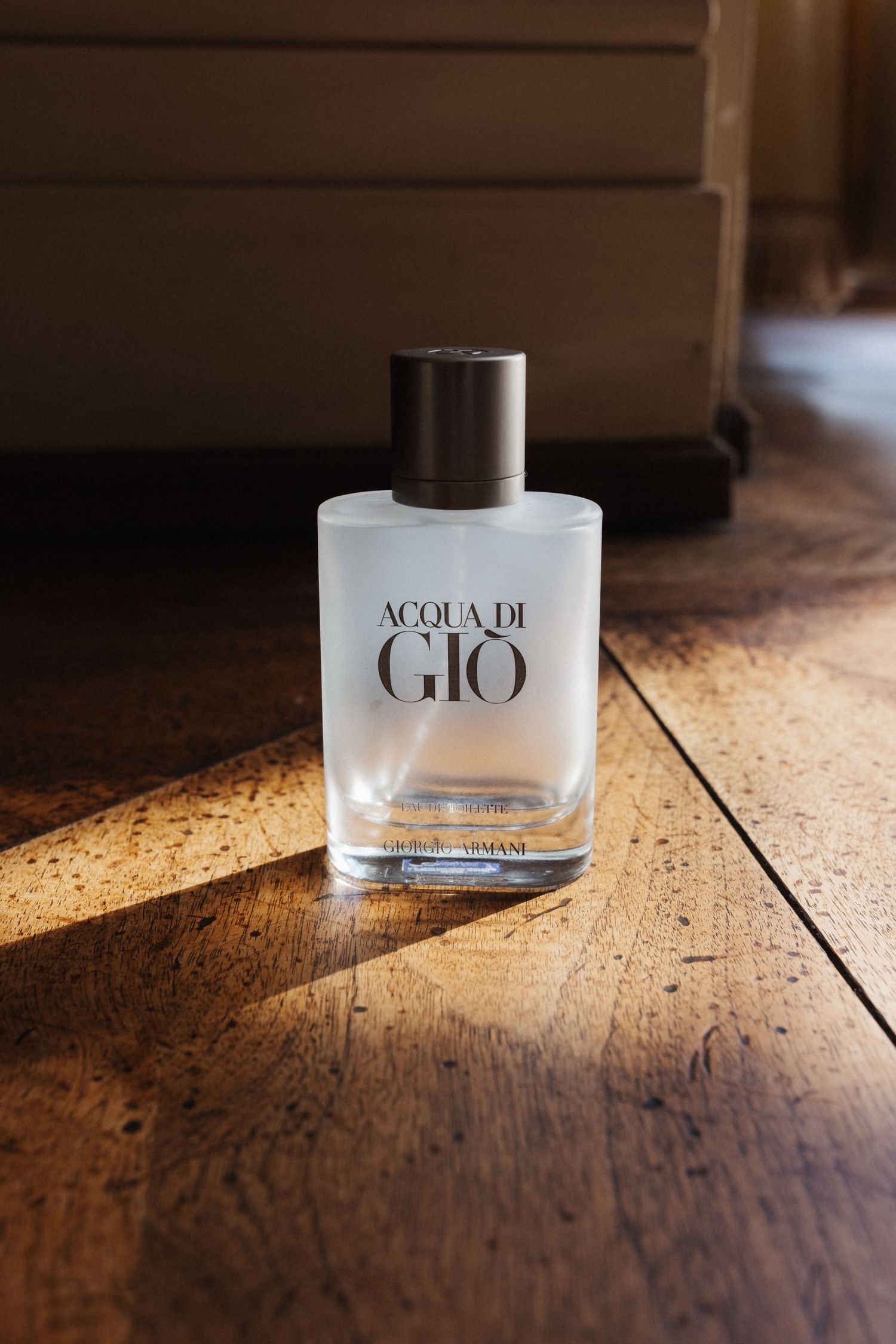 Acqua di Gio by Giorgio Armani cologne bottle on rustic wooden floor in warm sunlight.