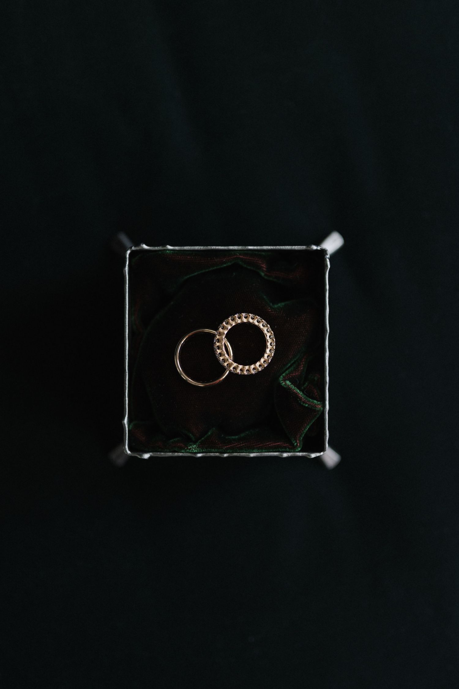 Two gold wedding rings nestled together in a dark jewelry box.