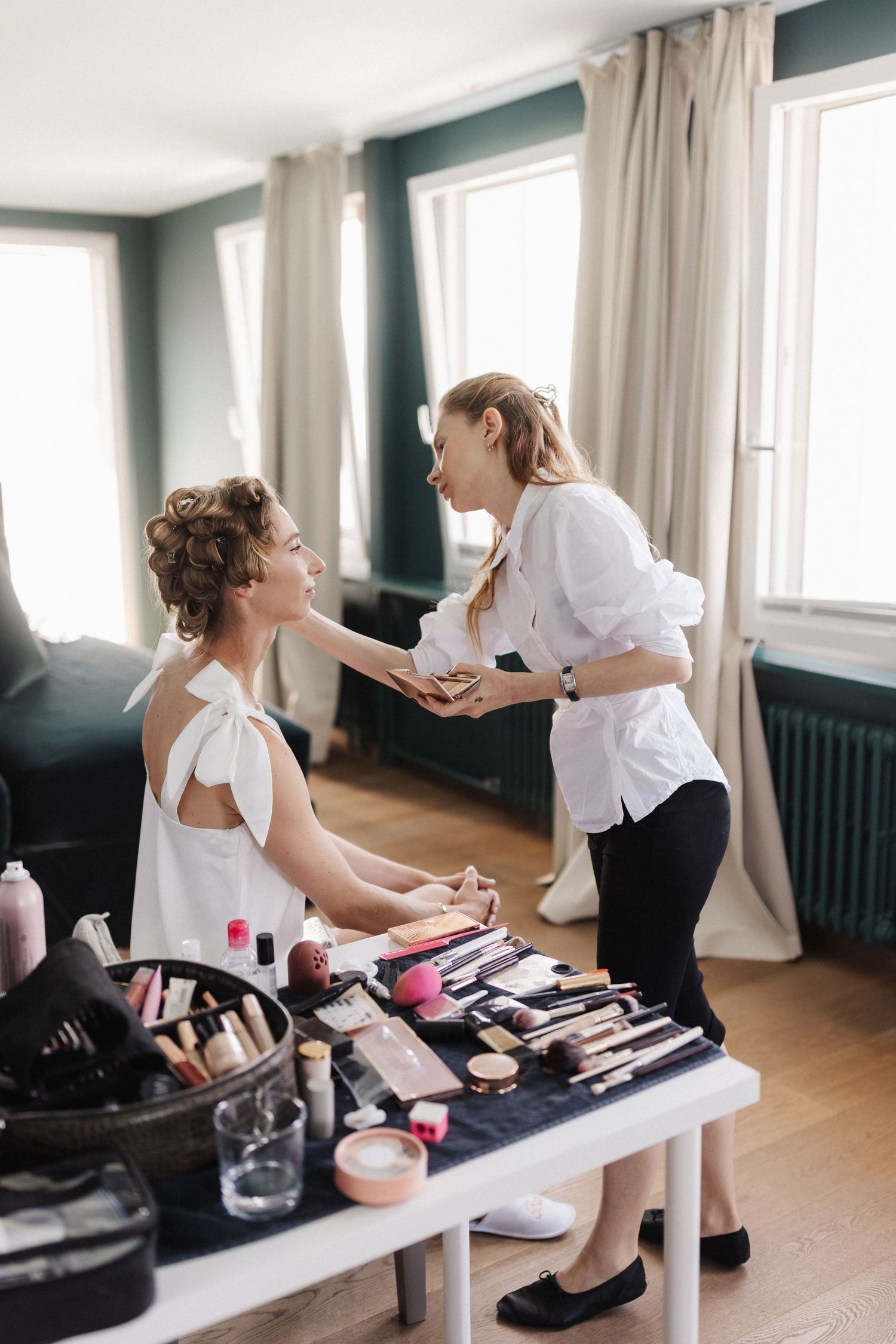 Professional makeup artist applying foundation to bride at vanity table.