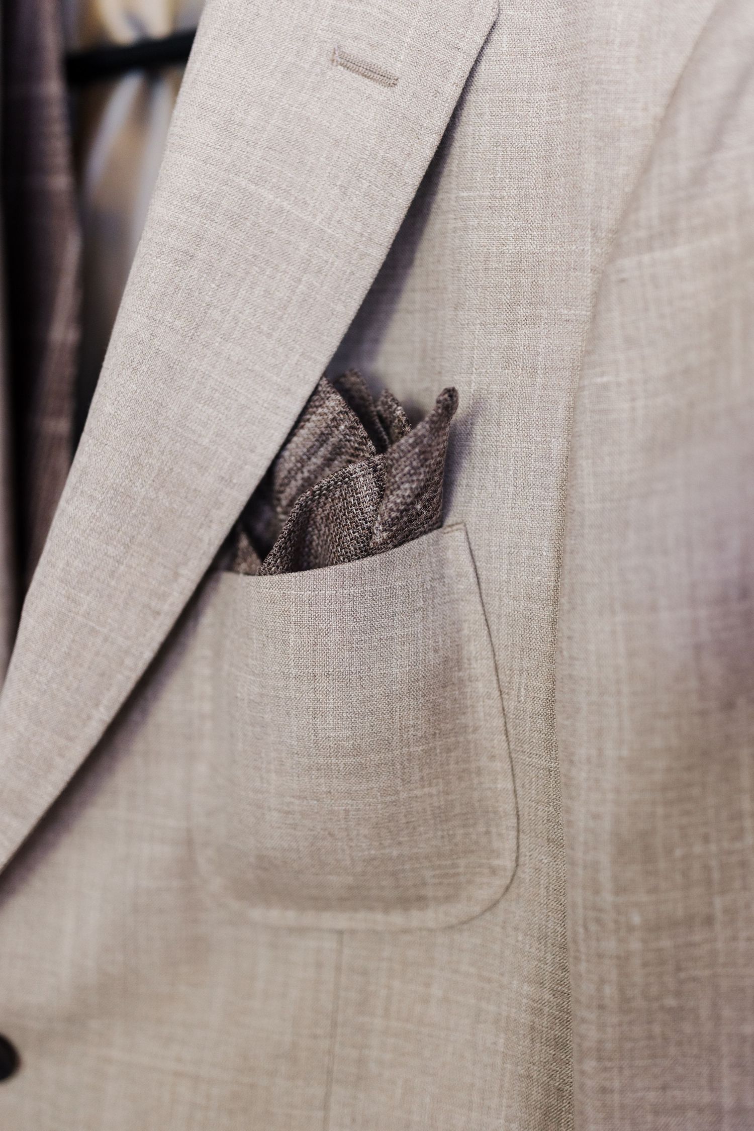 Close-up of a light beige textured suit jacket with a brown patterned pocket square.