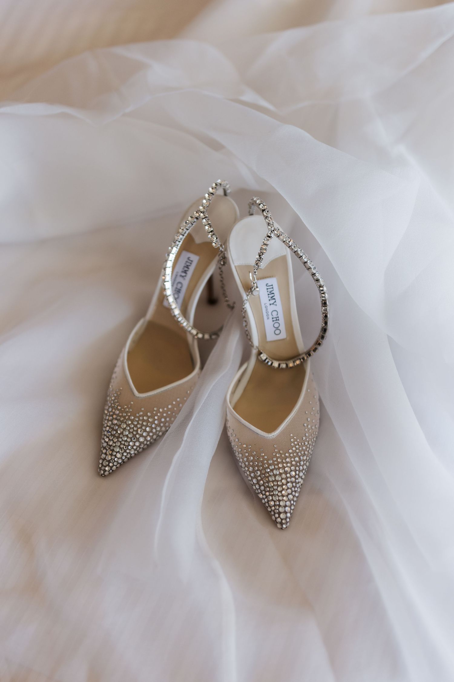 Pair of Jimmy Choo crystal-embellished slingback heels on white bridal veil fabric.