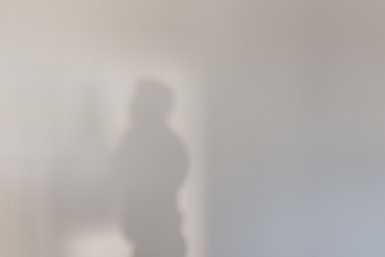 Soft silhouette shadow of a person standing against a light gray wall.