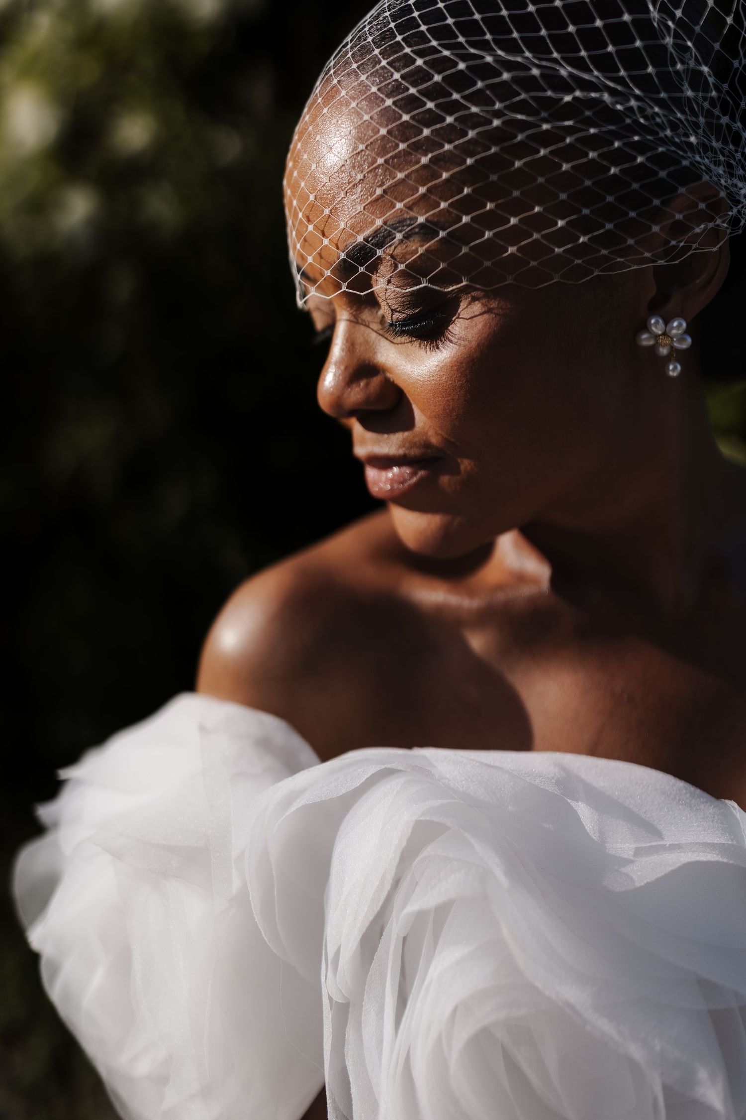 Close-up portrait of a bride in a birdcage veil and white ruffled gown with crystal drop earrings.