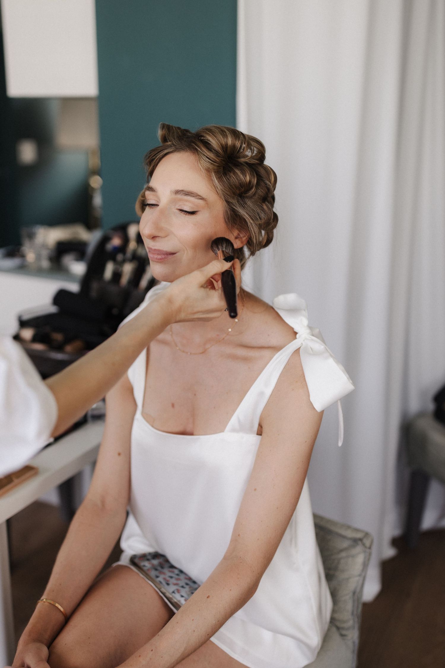 Bride with elegant updo receiving makeup application with large brush.