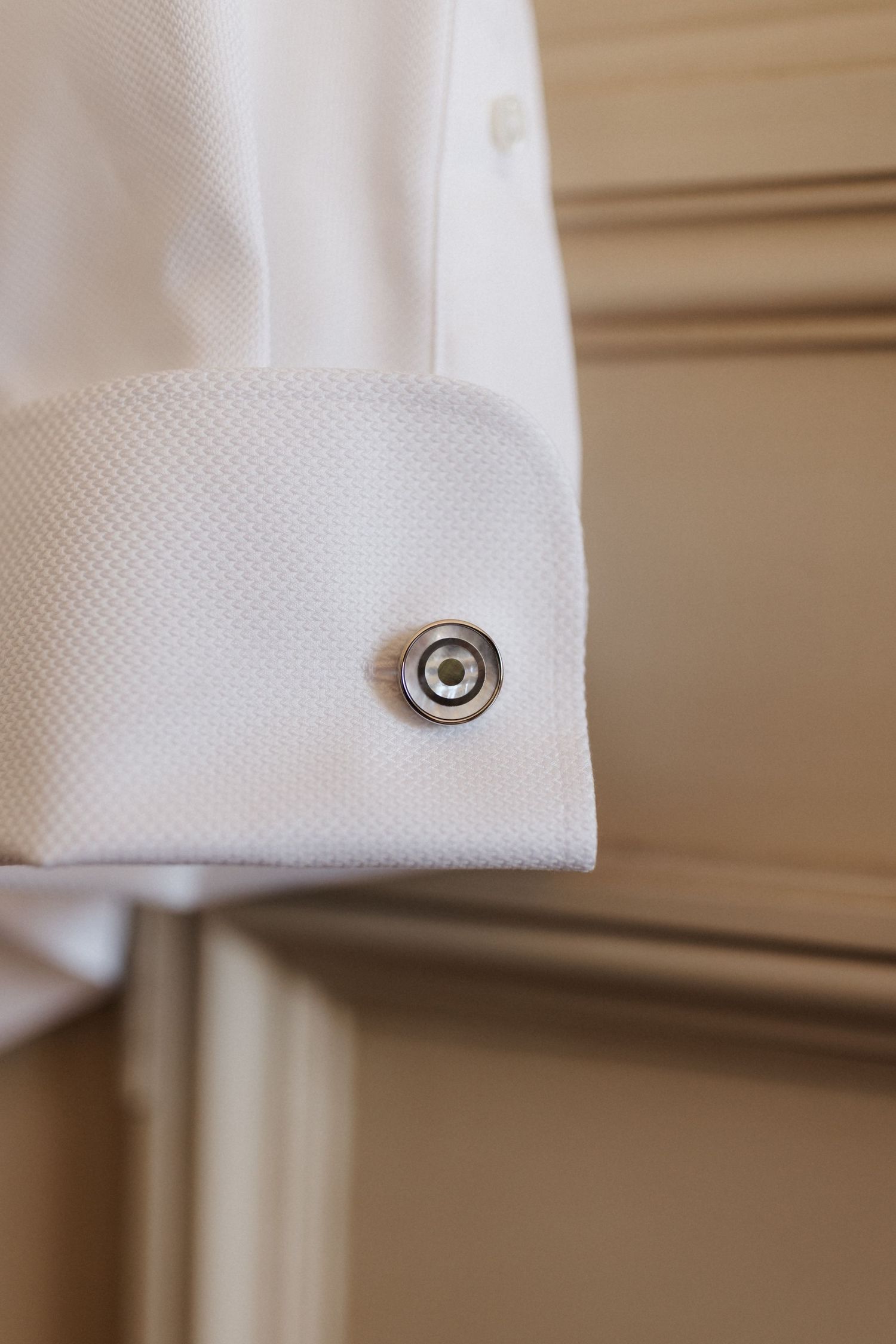 Close-up of white dress shirt French cuff with circular silver cufflink against wooden molding.