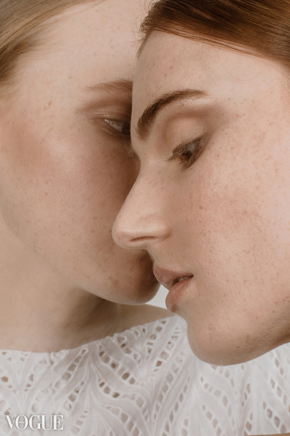 Intimate close-up profile of two freckled women with red hair facing each other in white tops.