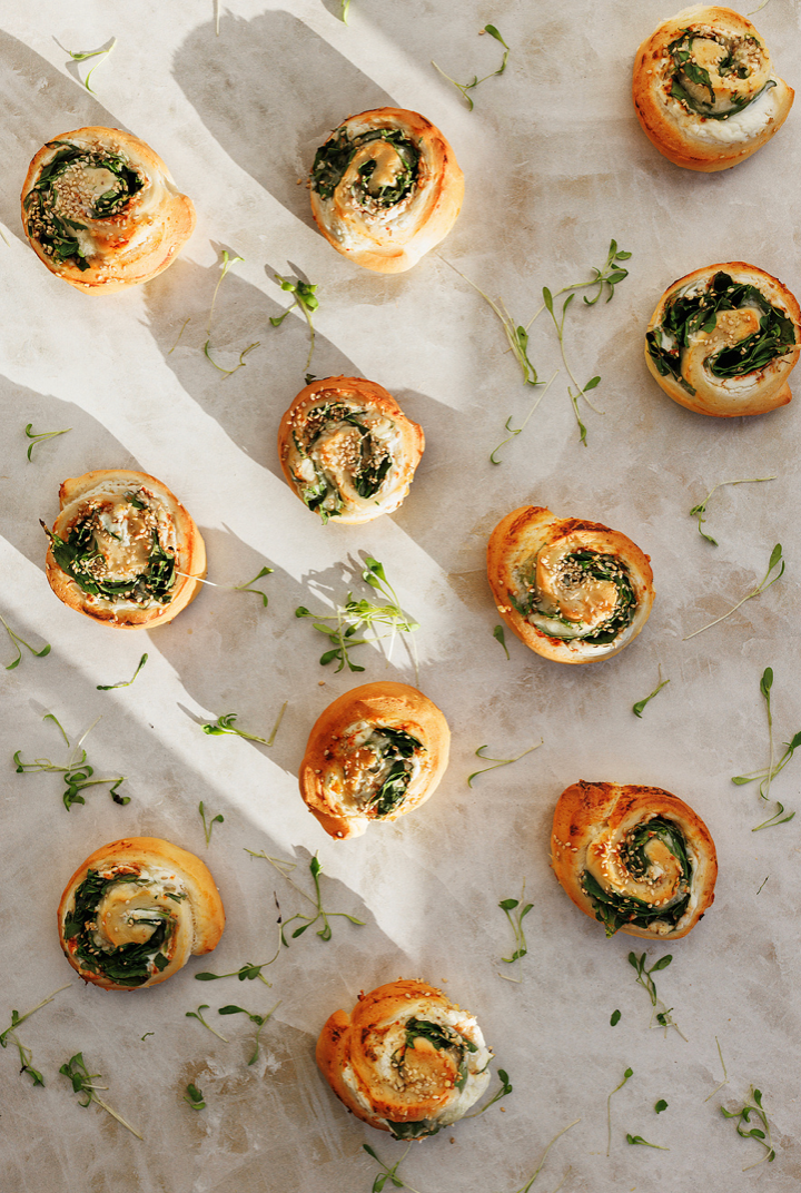 Flat lay of spinach and cheese pinwheel pastries scattered on parchment with fresh herbs.