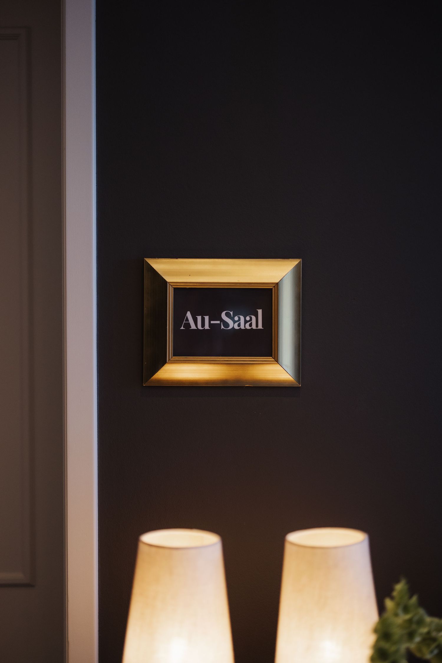 Elegant gold-framed Au-Saal sign on dark wall illuminated by two warm table lamps.