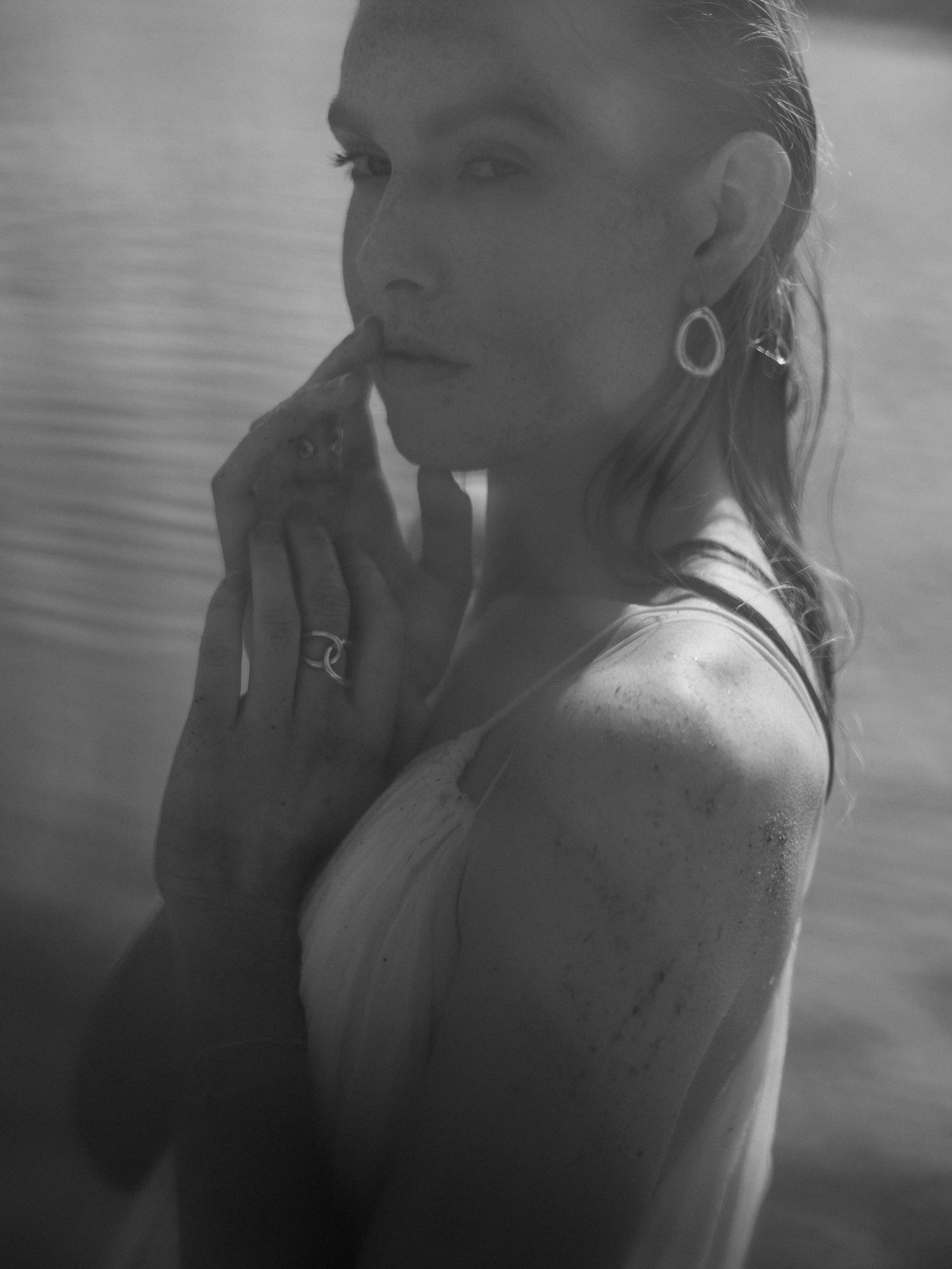 Black and white portrait of wet woman with slicked back hair wearing hoop earrings and rings.