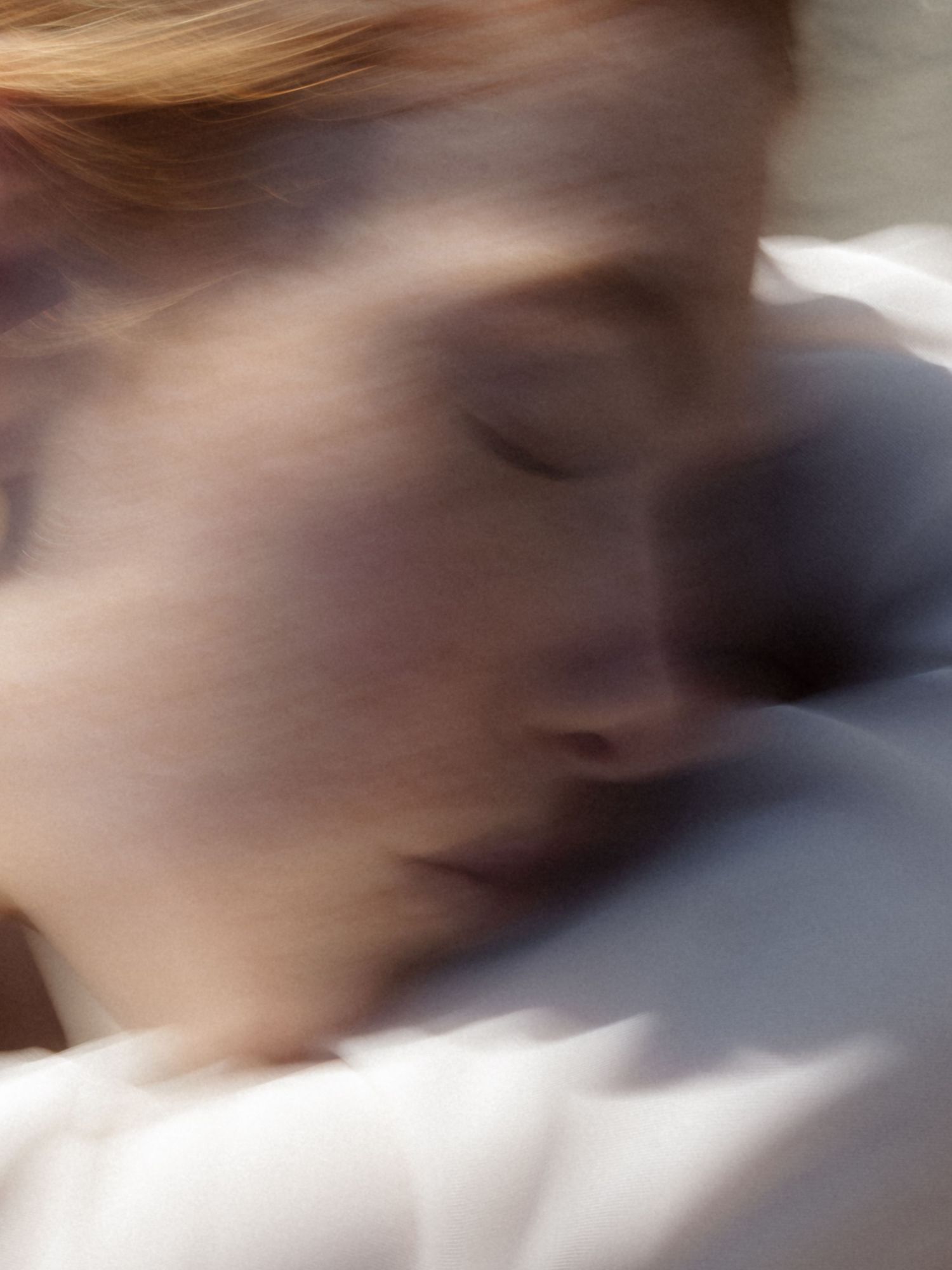 Soft blurred portrait of a red-haired woman resting peacefully with eyes closed.