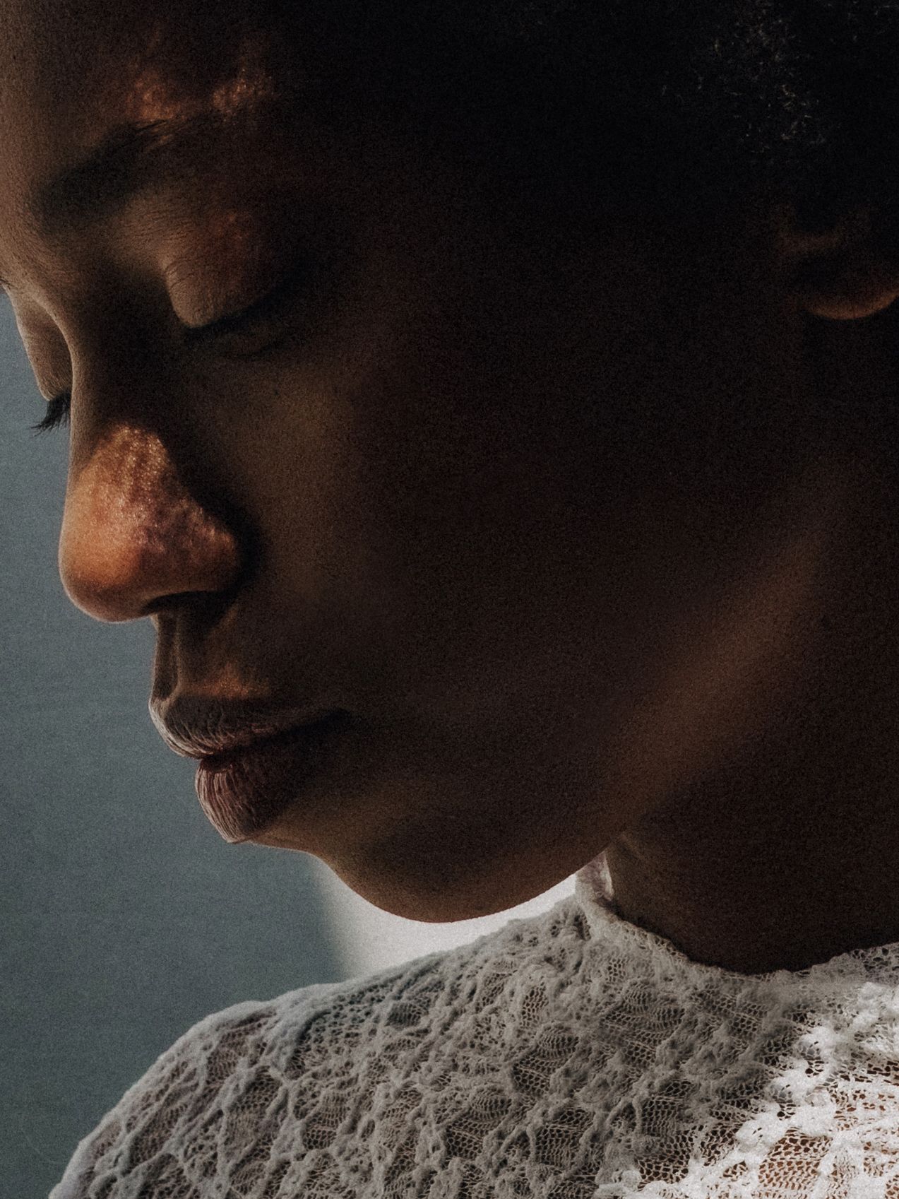Close-up profile portrait of woman in white lace top with dramatic moody lighting.