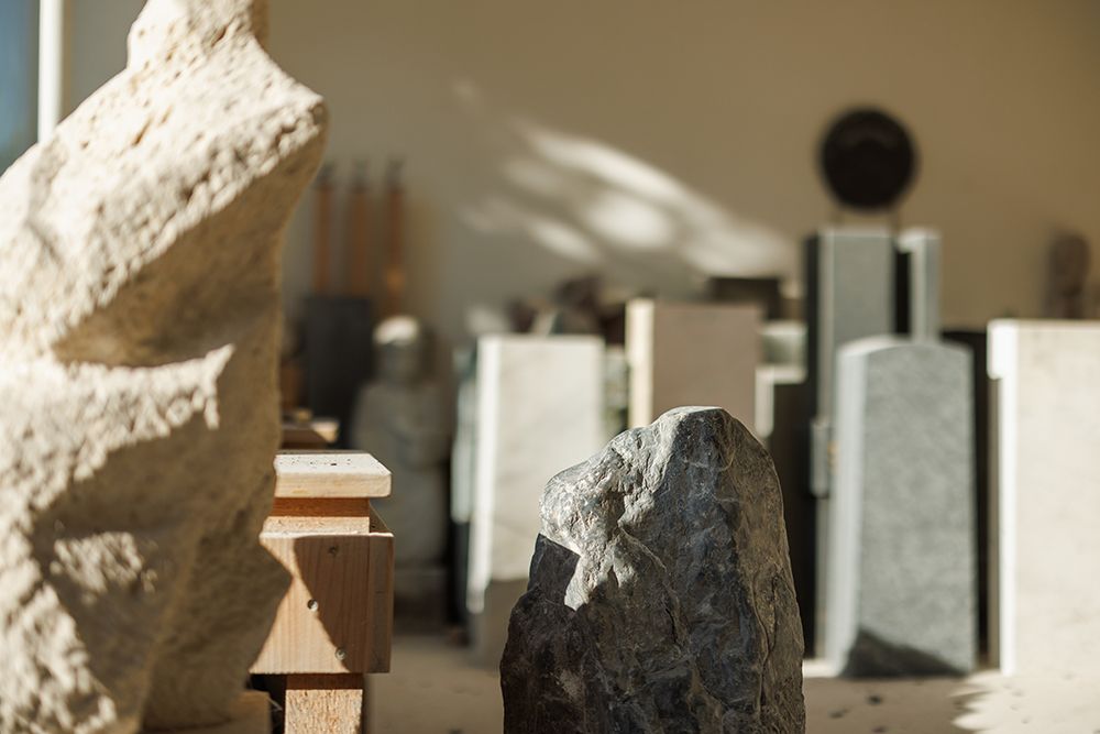 Stone sculptor's studio with rough limestone and dark granite rocks in warm natural sunlight.