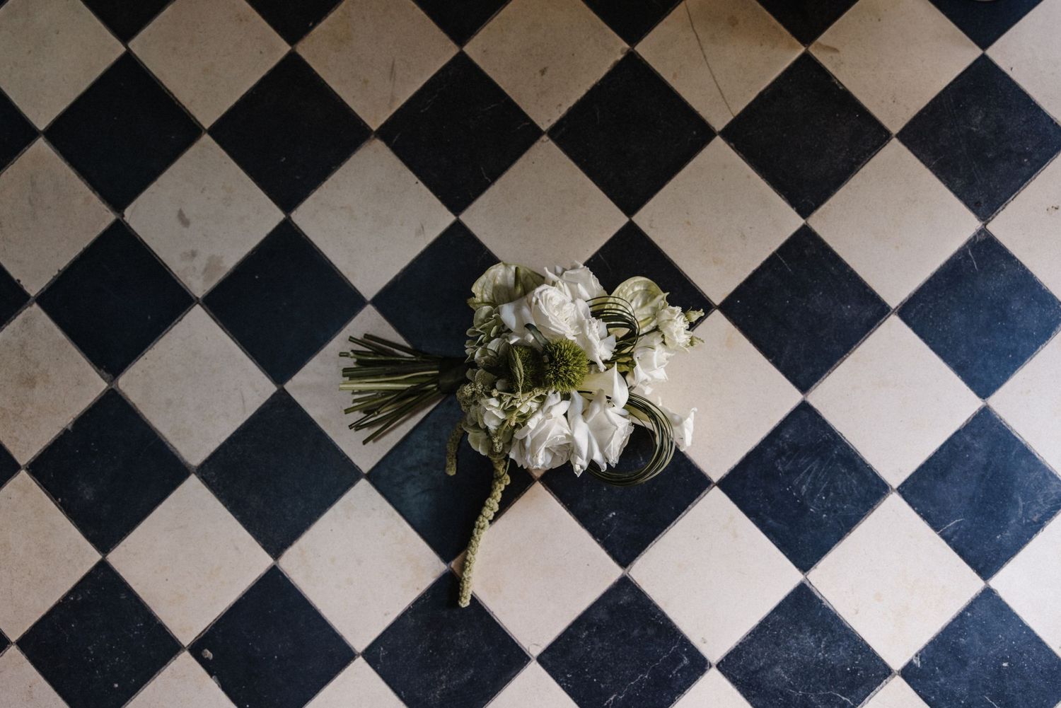 White wedding bouquet with roses placed on classic black and white checkered tile floor.