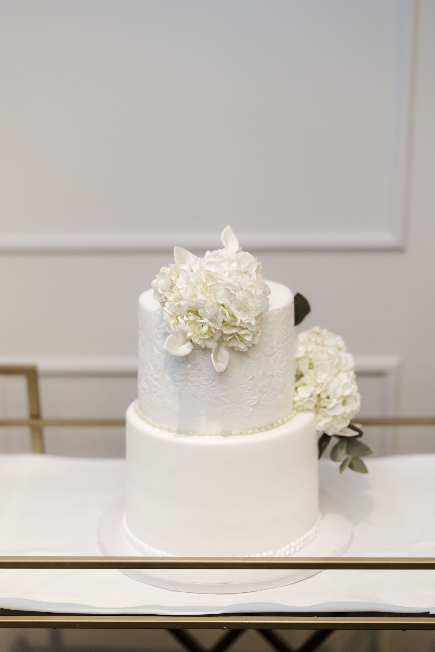 Elegant two-tier white wedding cake decorated with white hydrangea flowers on a marble table.