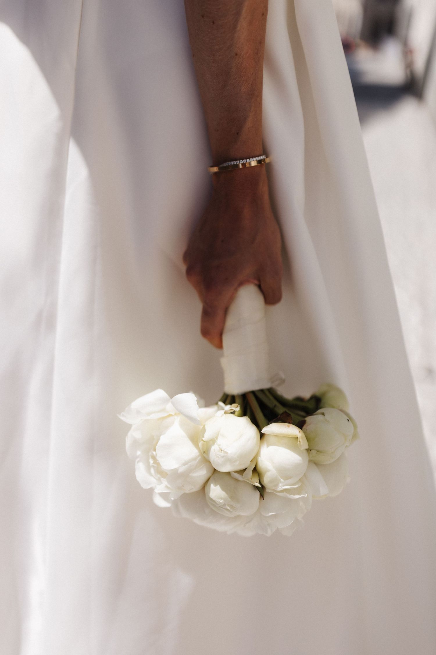 A bride in white holds a delicate bouquet of white tulips at her side, with a gold bracelet visible.