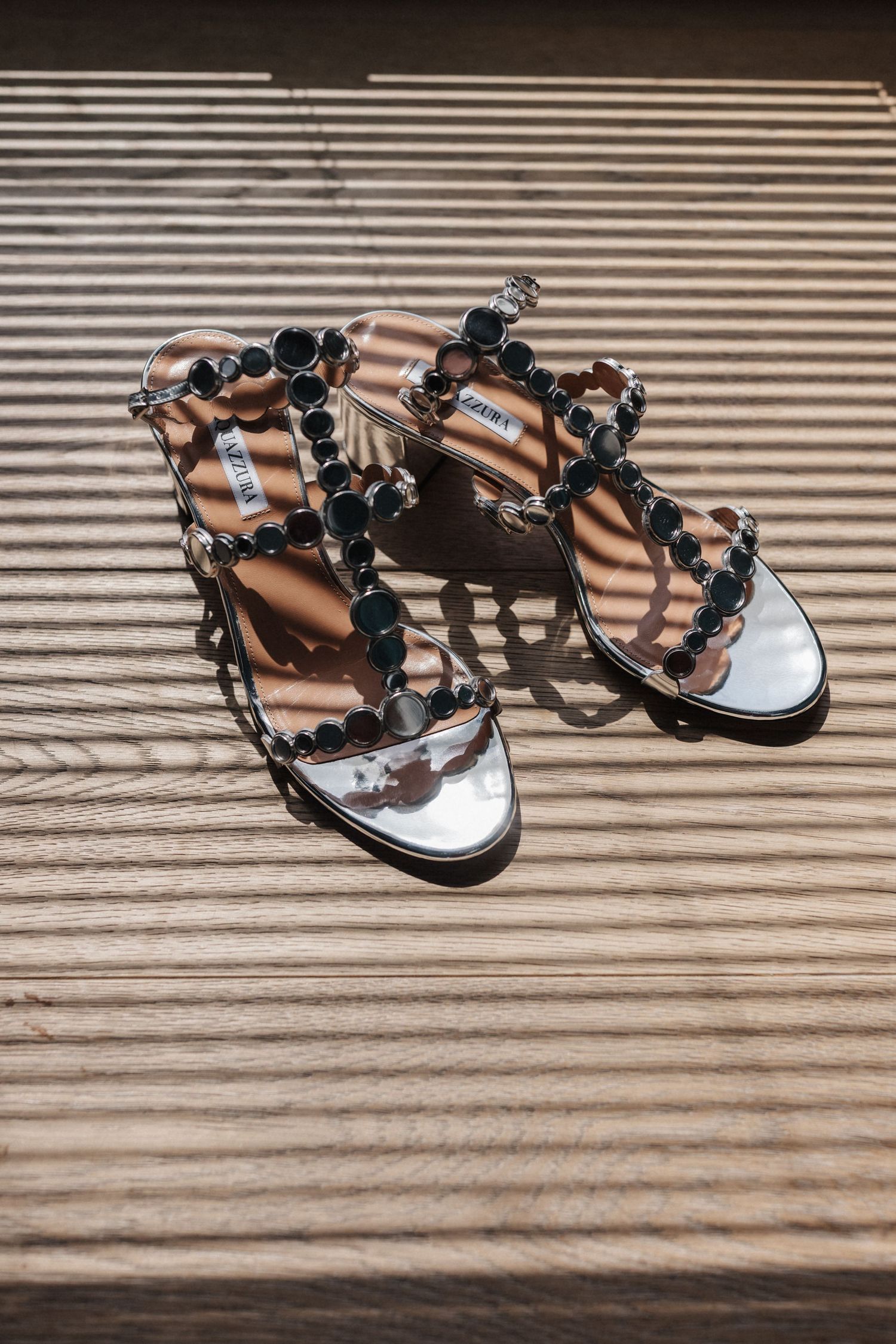 Silver jeweled bridal sandals with circular embellishments on wooden surface.
