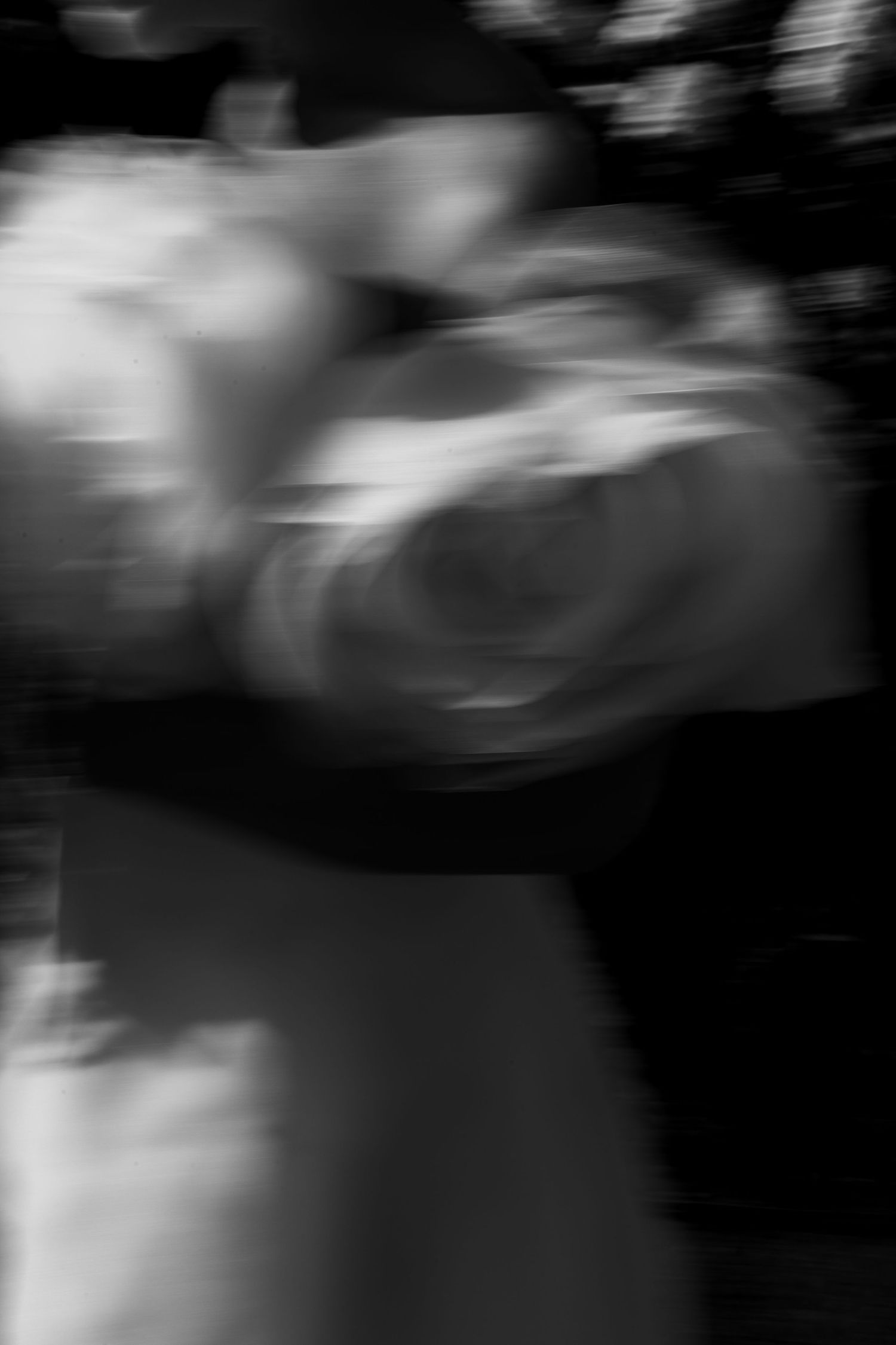 Artistic blurred black and white motion shot of a bride holding a white floral bouquet outdoors.