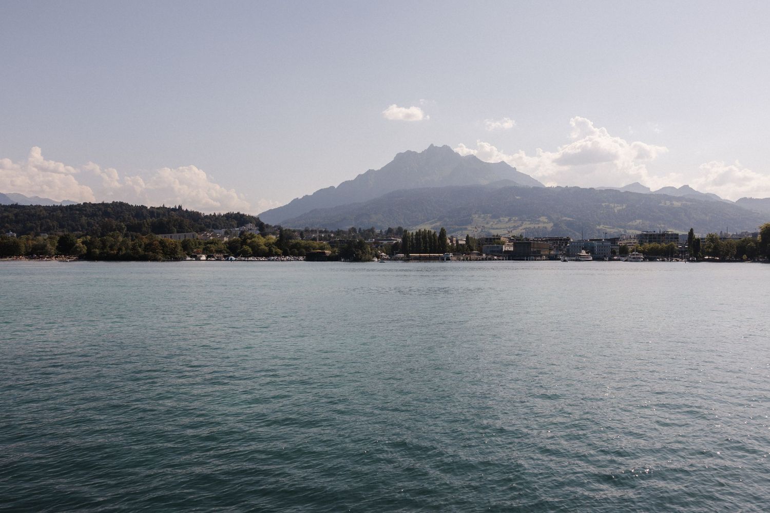 Panoramic view of a Swiss alpine lake with turquoise water and mountain peaks visible on a sunny day.