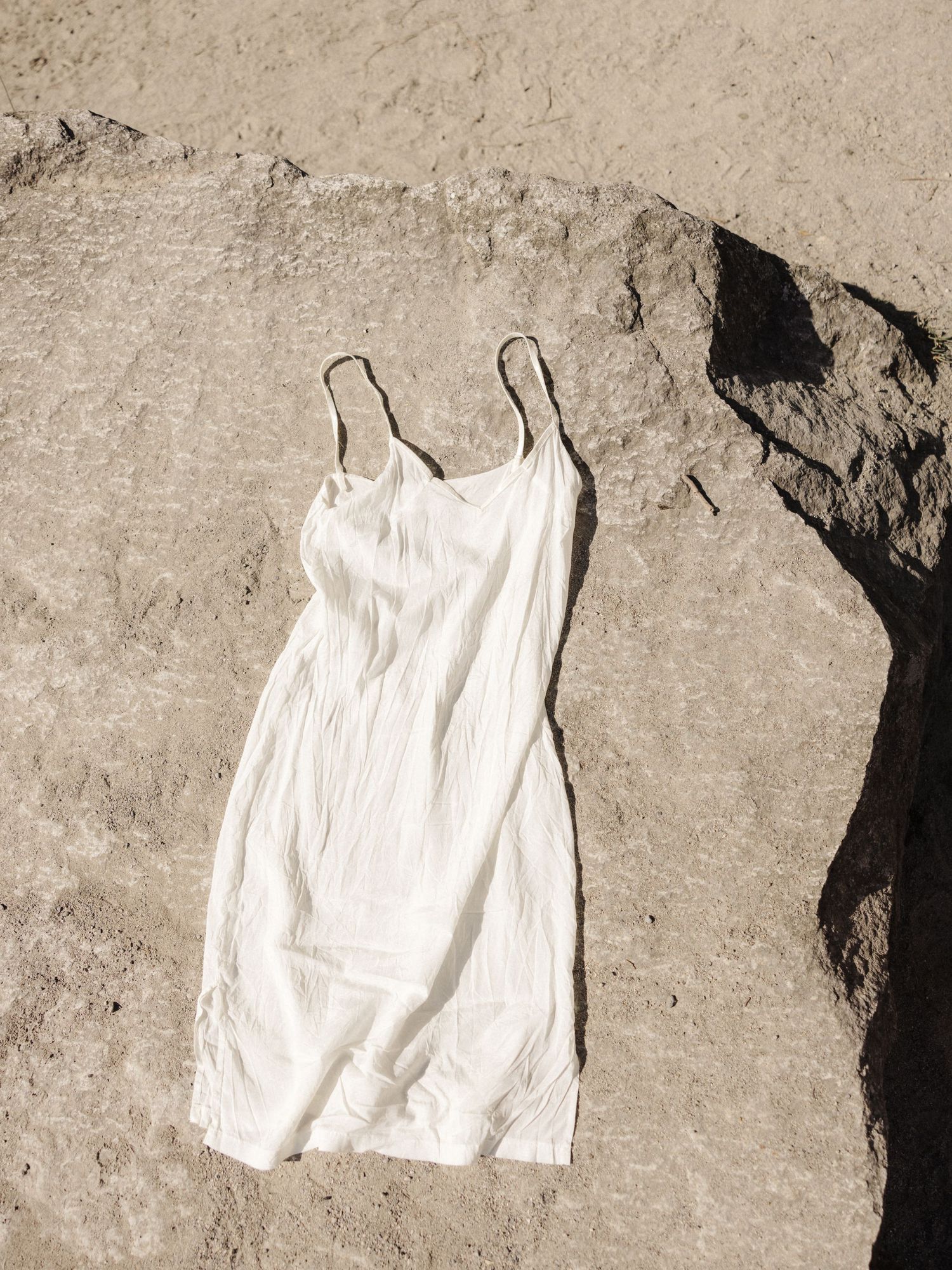 White slip dress laid flat on rocky stone surface in bright sunlight.
