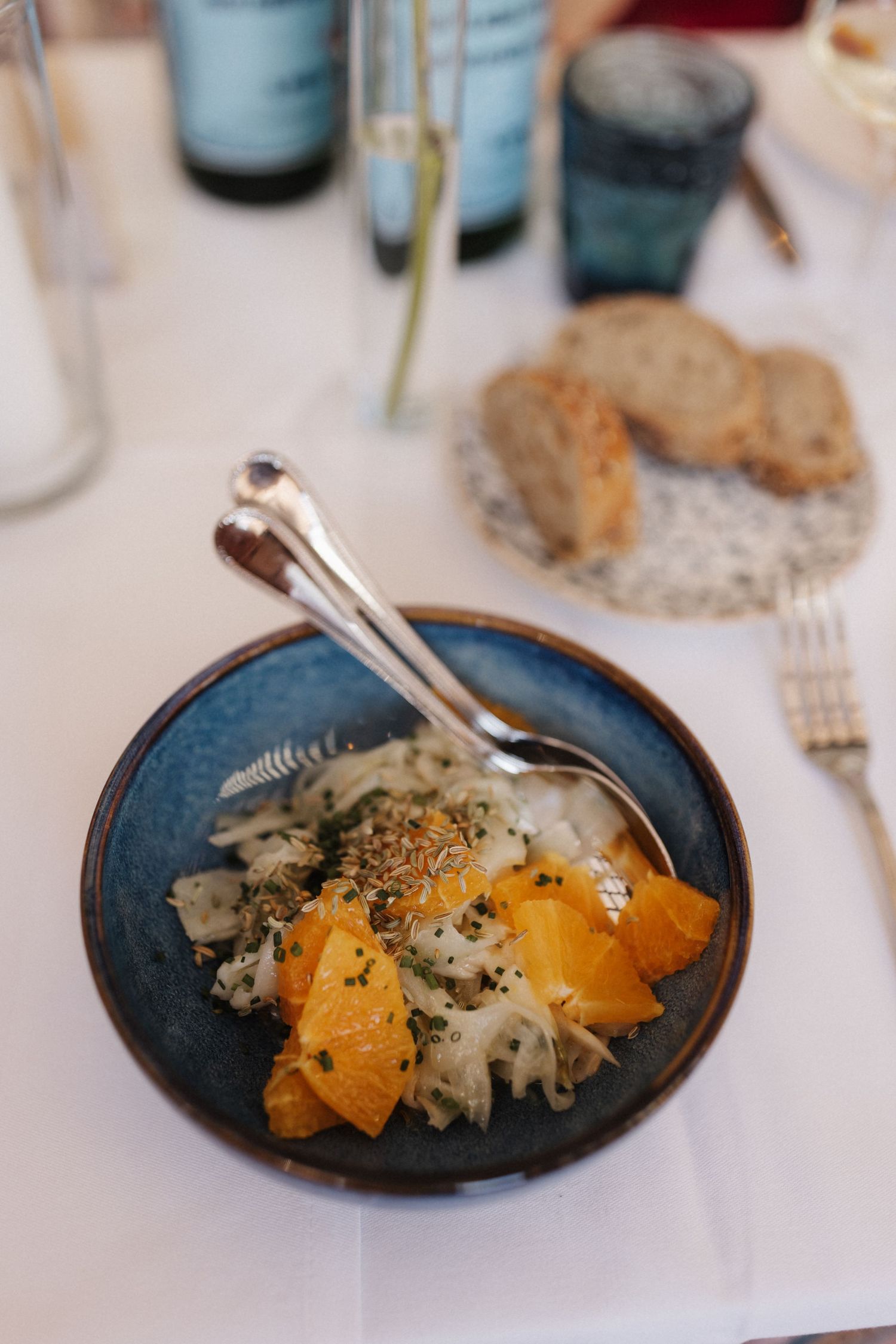 A blue ceramic bowl with fennel orange salad served alongside bread at a wedding reception.
