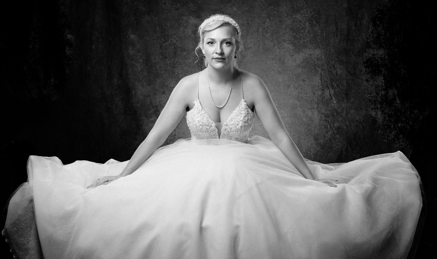 Stunning bride in flowing ballgown poses for artistic black and white bridal portrait photo.