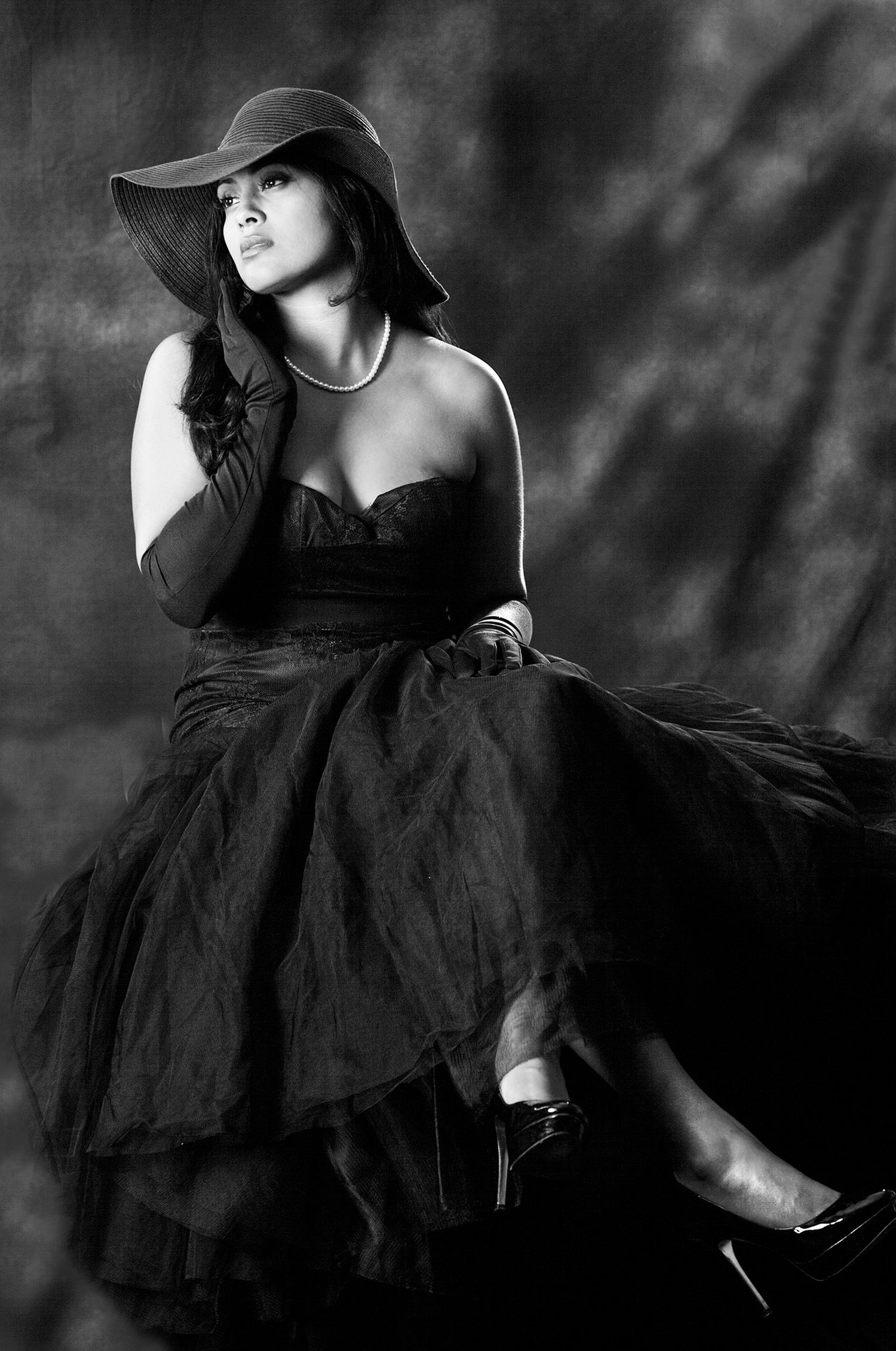 Elegant woman in black strapless gown and wide brim hat posing in black and white.