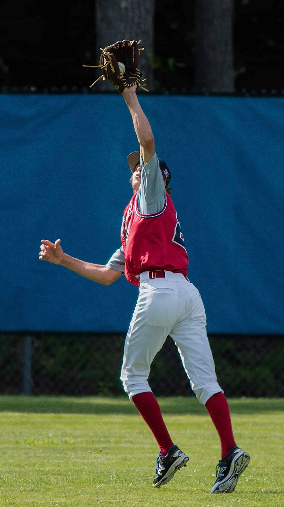 Baseball outfielder in red uniform leaping to catch a fly ball with glove raised high on a sunny day.
