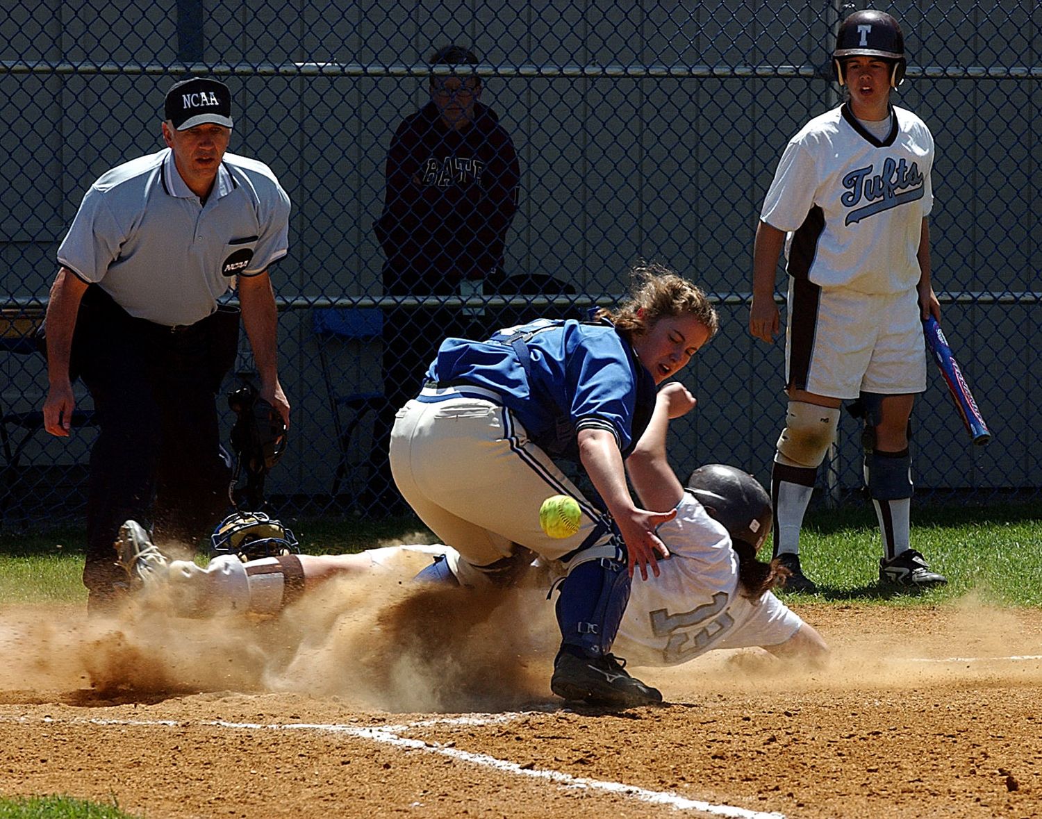 Softball player sliding into home plate in a cloud of dust as catcher attempts tag, with umpire watching closely.