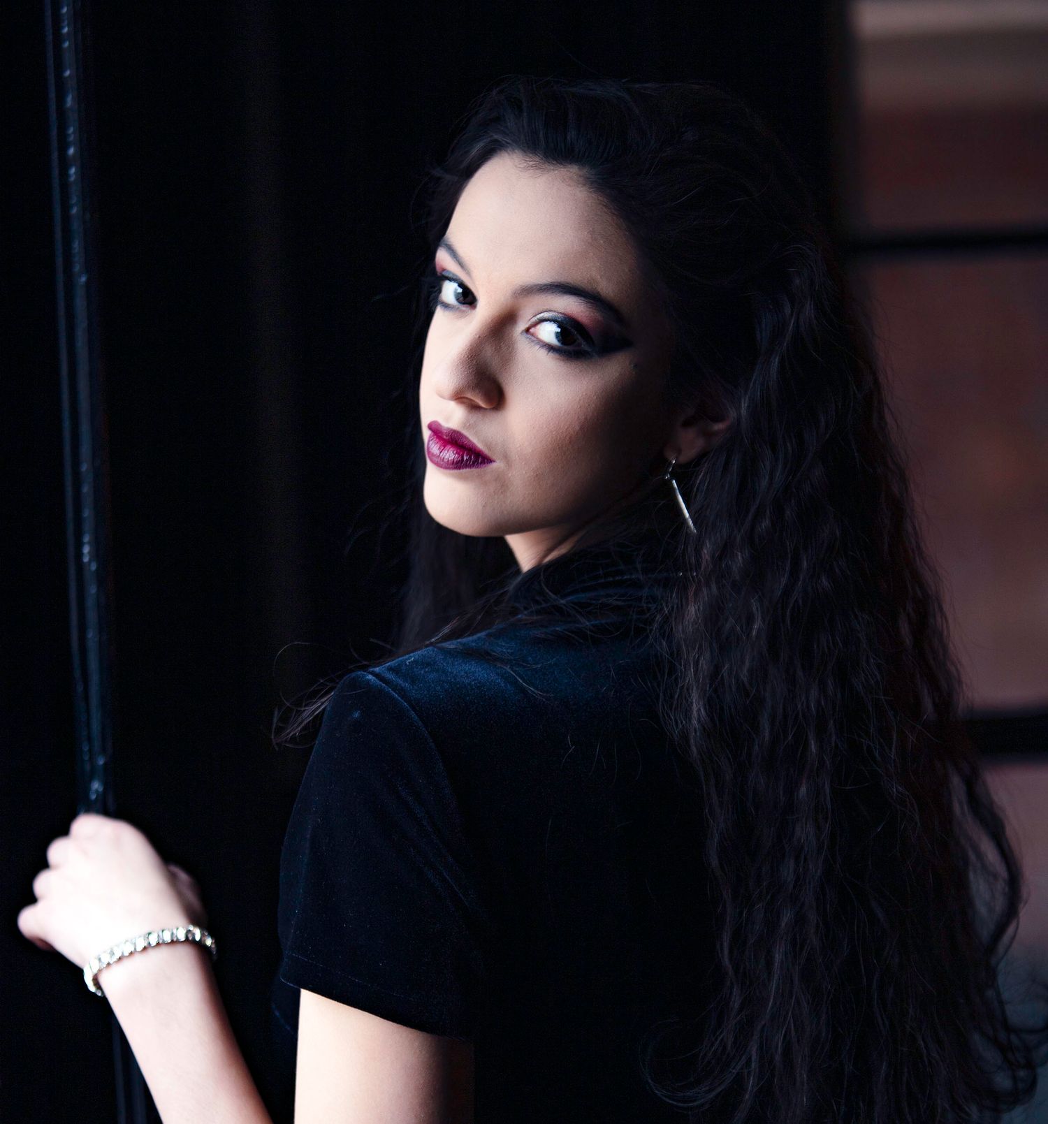 Young woman with long dark hair and bold makeup wearing black, posing with a dramatic look.