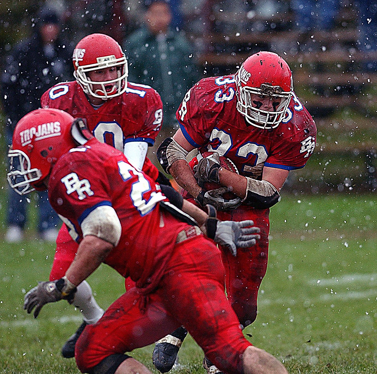 Red-uniformed Trojans football players compete in a snowy game, with number 33 carrying the ball through defenders.