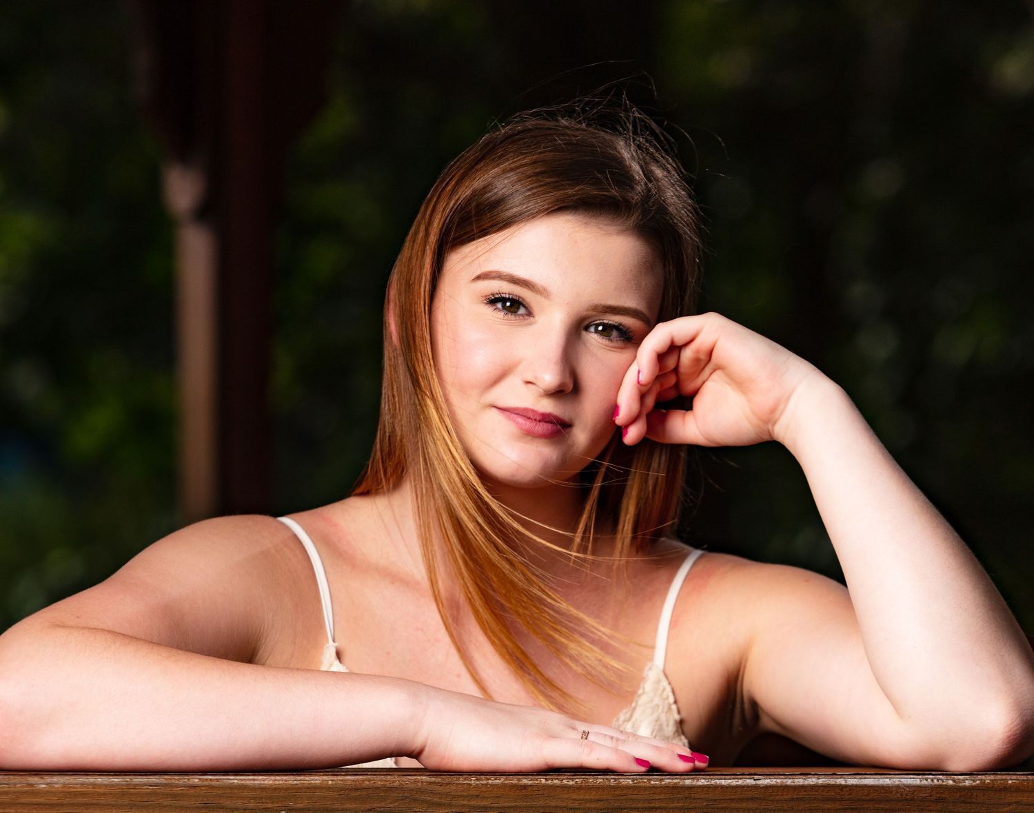 Teen girl with auburn hair resting chin on hand for relaxed outdoor senior portrait photo.