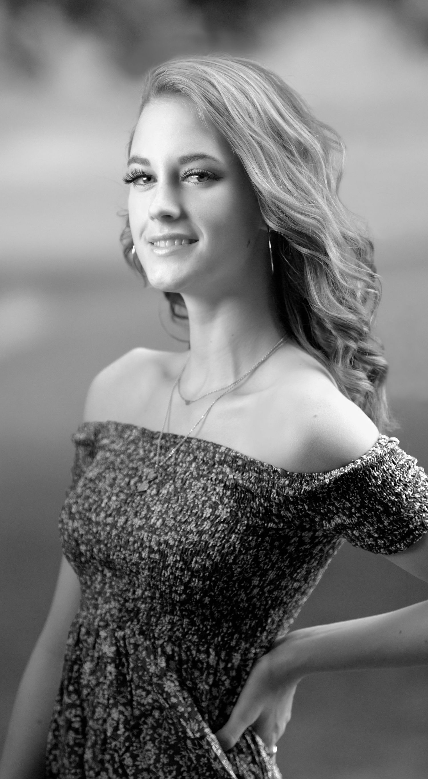 Black and white portrait of teenage girl in off-shoulder dress with wavy blonde hair.