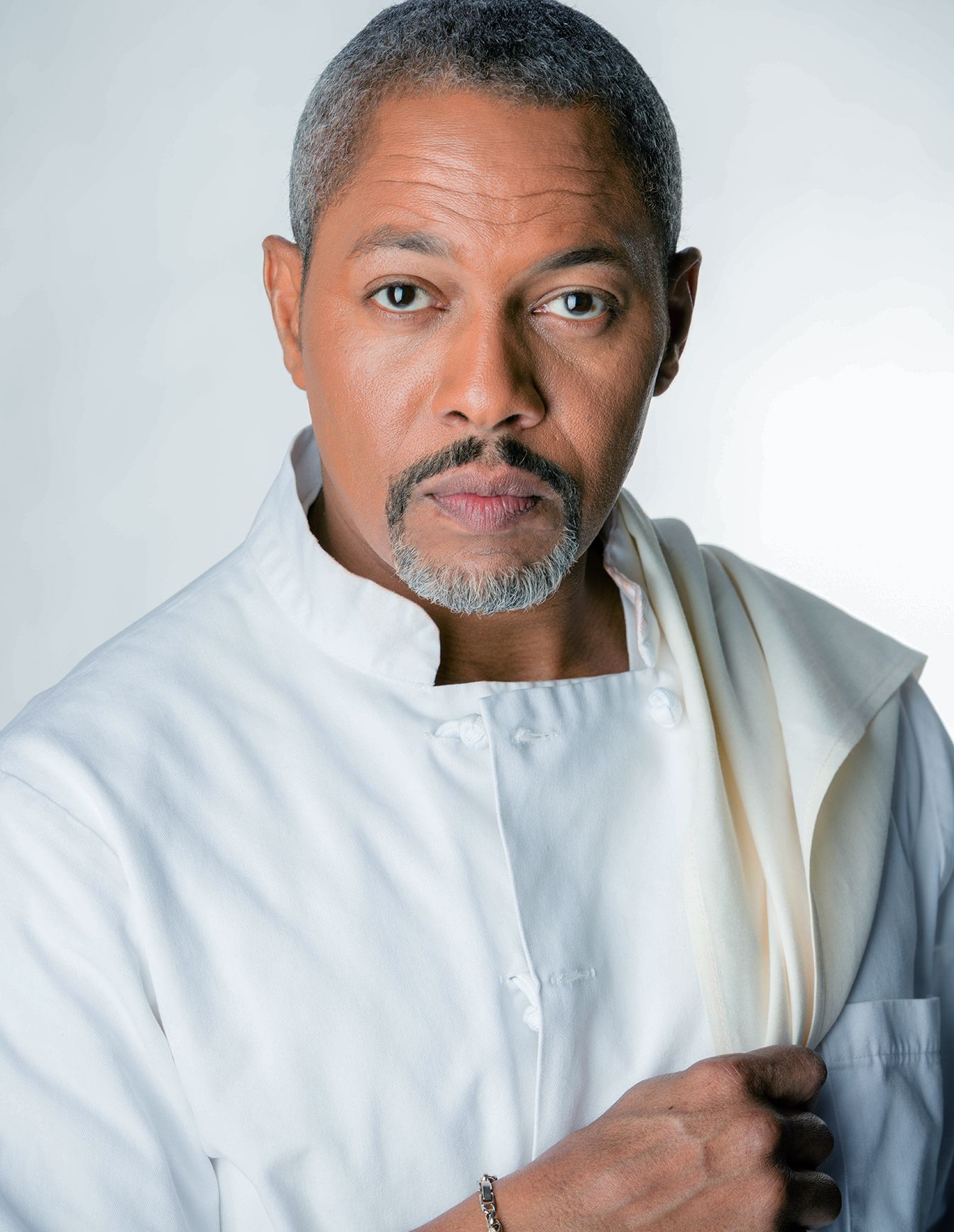Professional chef in white uniform posing confidently for a portrait photo against a light background.