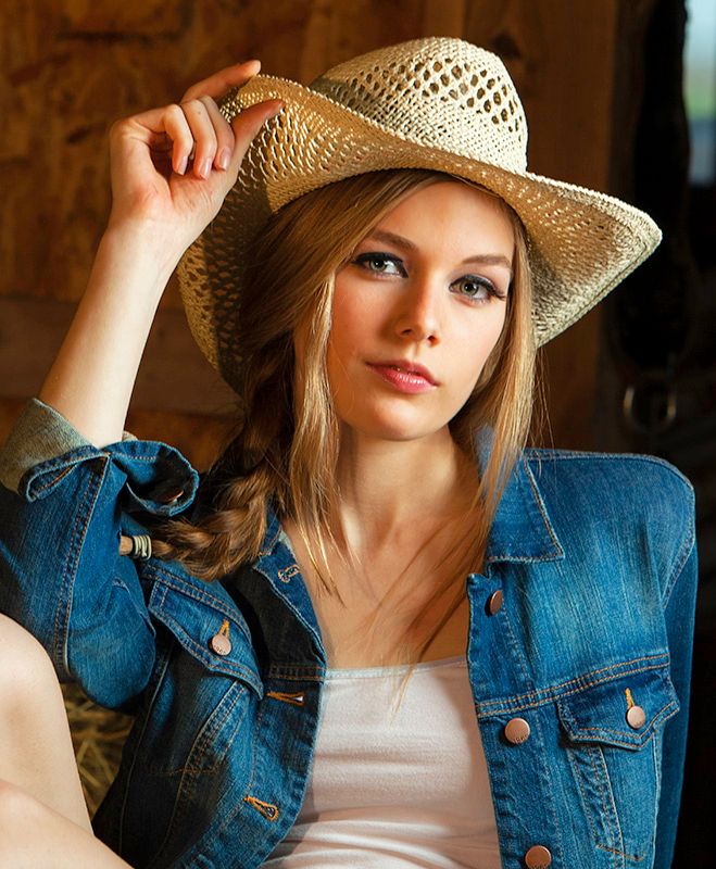 Young blonde woman in denim jacket and straw cowboy hat posing for portrait photo.