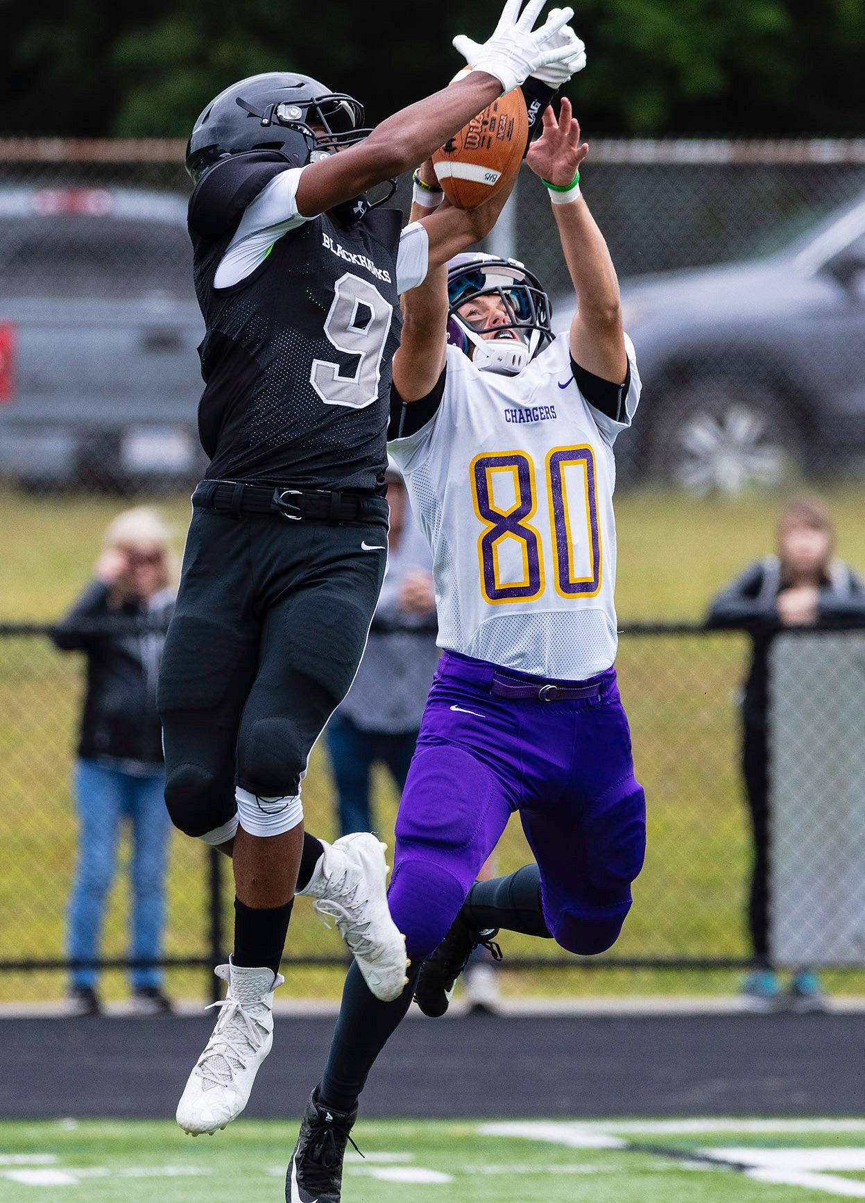 Two football players battle for a catch, player #9 in black and player #80 in white and purple uniforms.