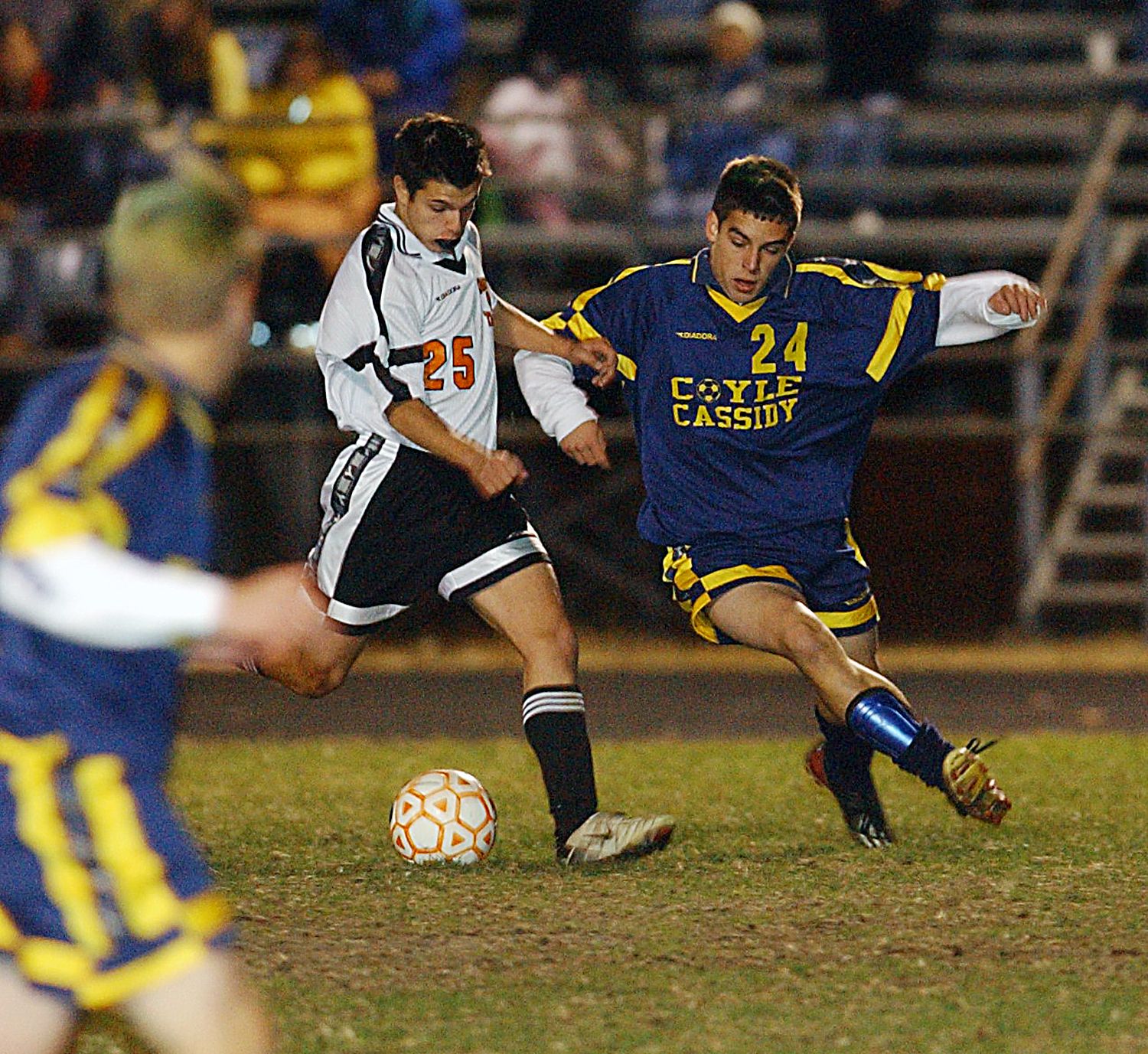 Two soccer players compete for the ball during a night game, wearing jerseys numbered 25 and 24 for Coyle Cassidy.
